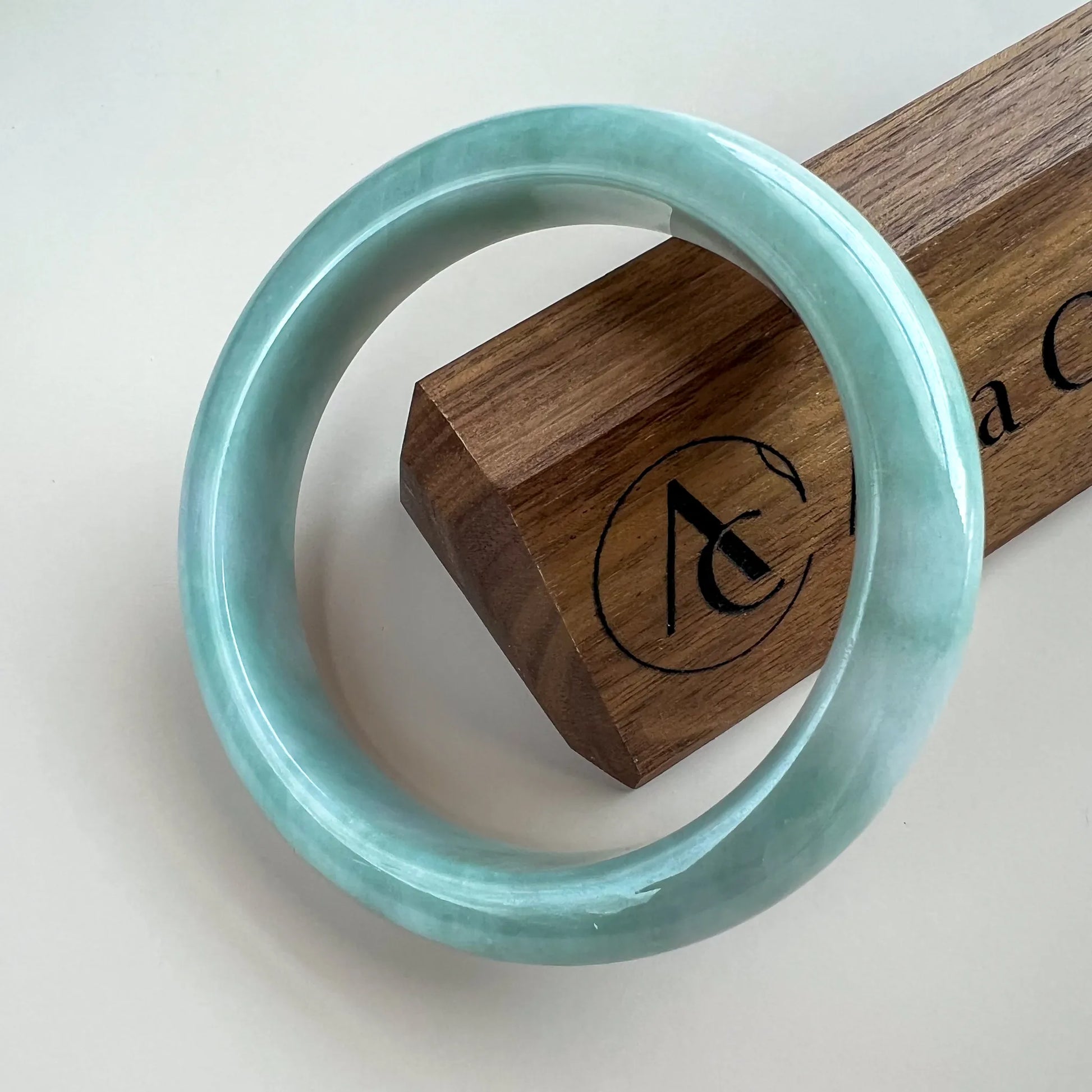 Glossy light green jade bangle angled on wooden stand, smooth polished round profile
