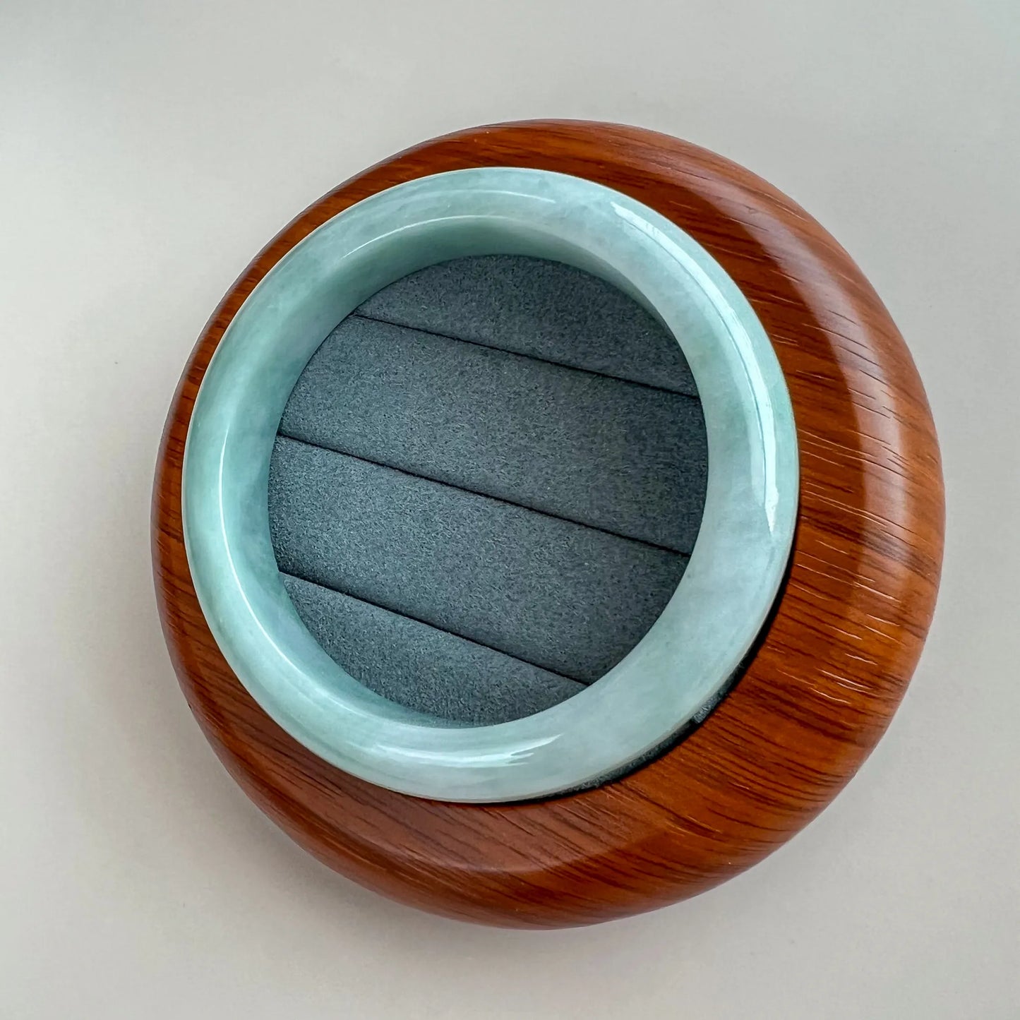 Jade bangle resting on wooden display base, top-down view with polished finish
