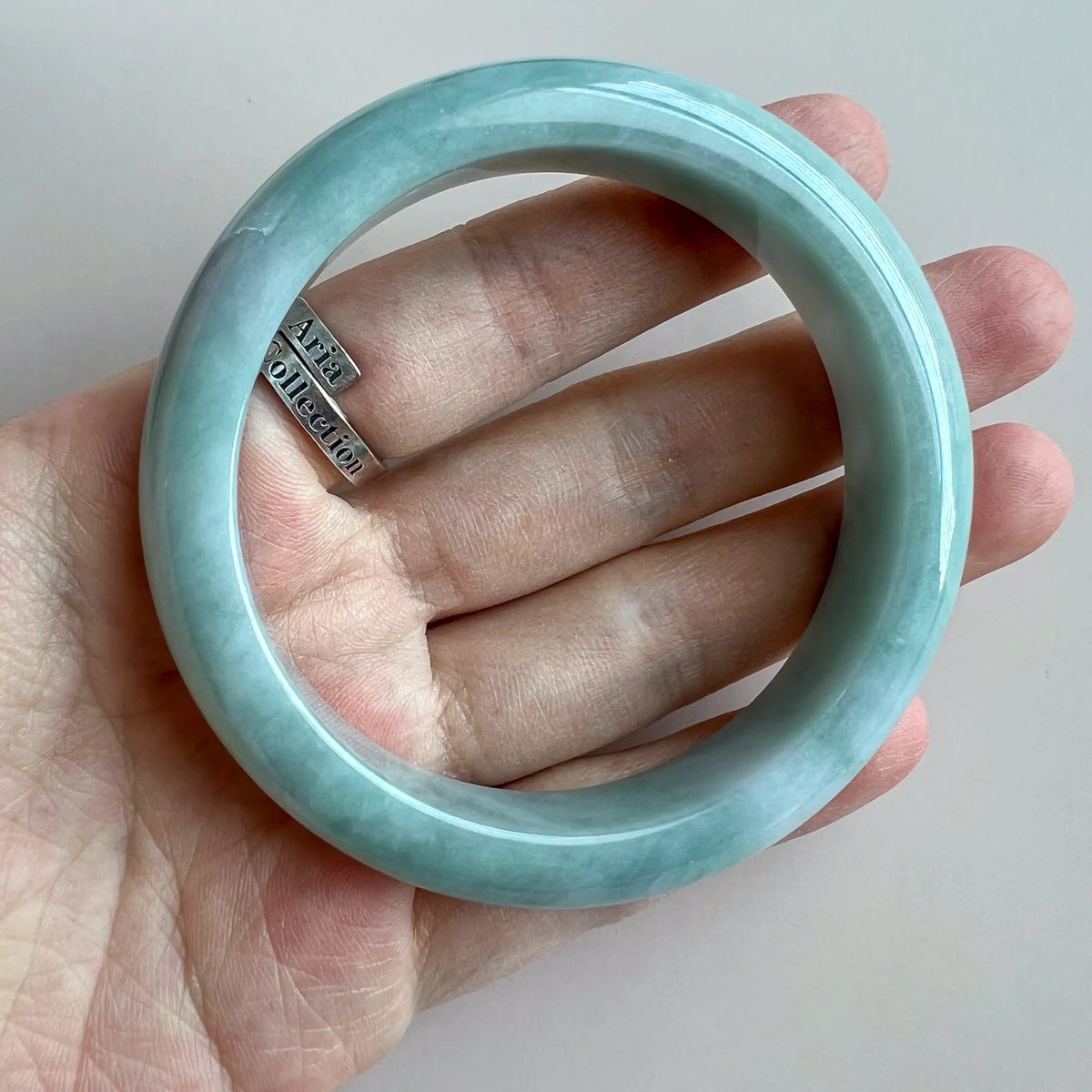 Polished jade bangle shown on hand for scale, translucent pale green stone