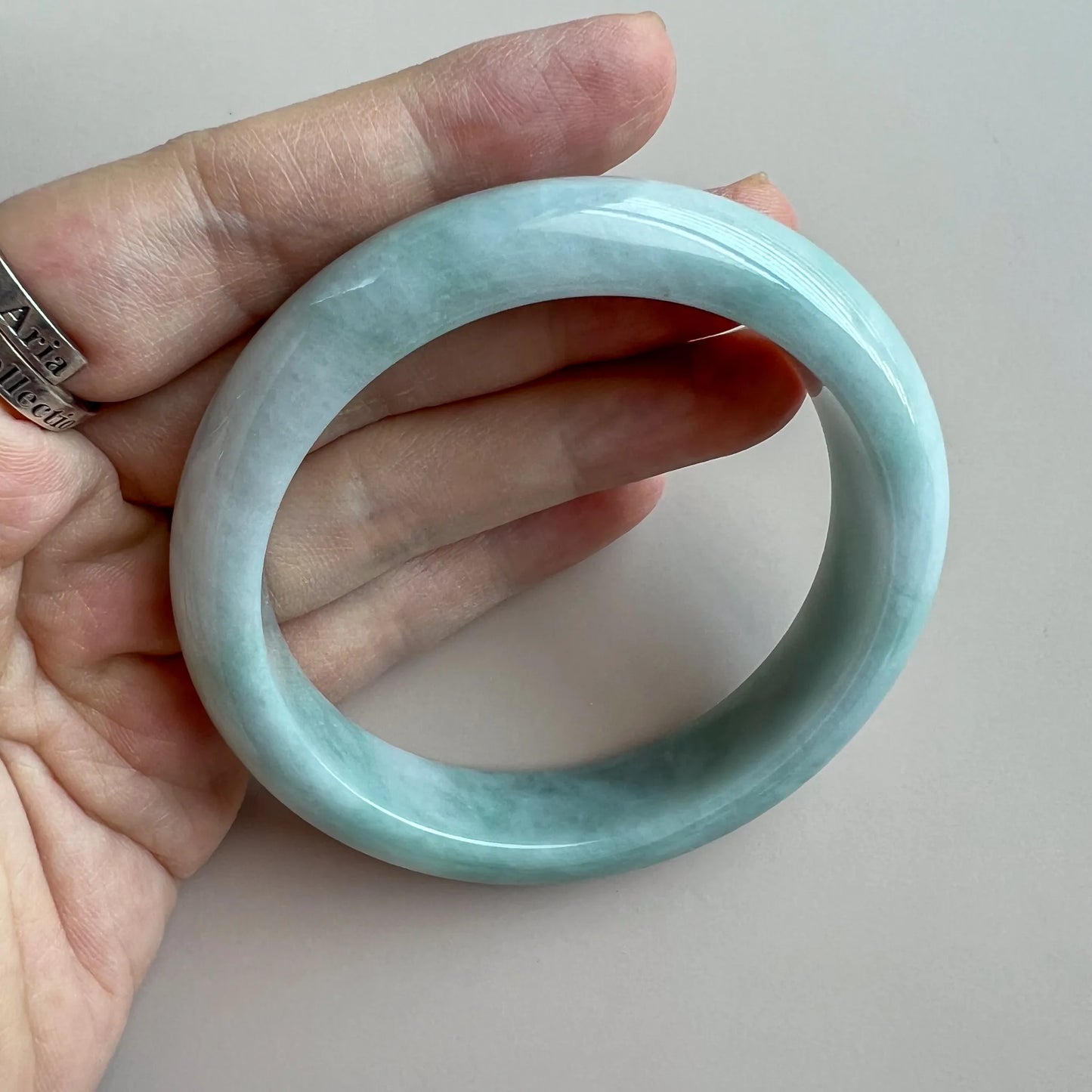 Side view of smooth jade bangle held in hand, glossy pale green finish