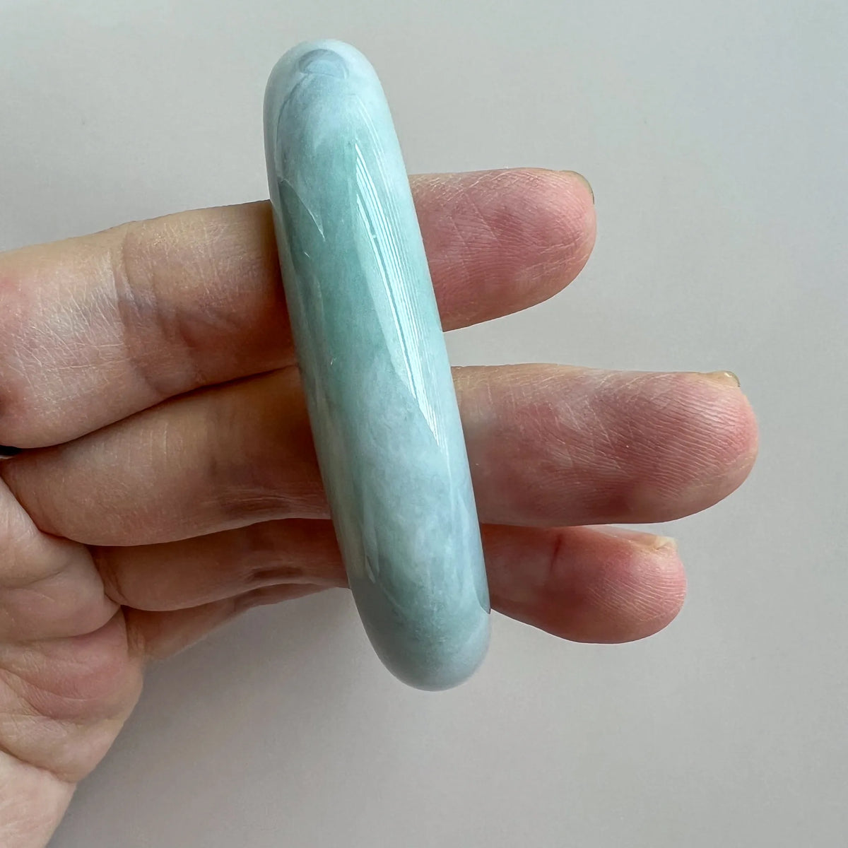 Edge profile of jade bangle held upright, rounded polished stone surface