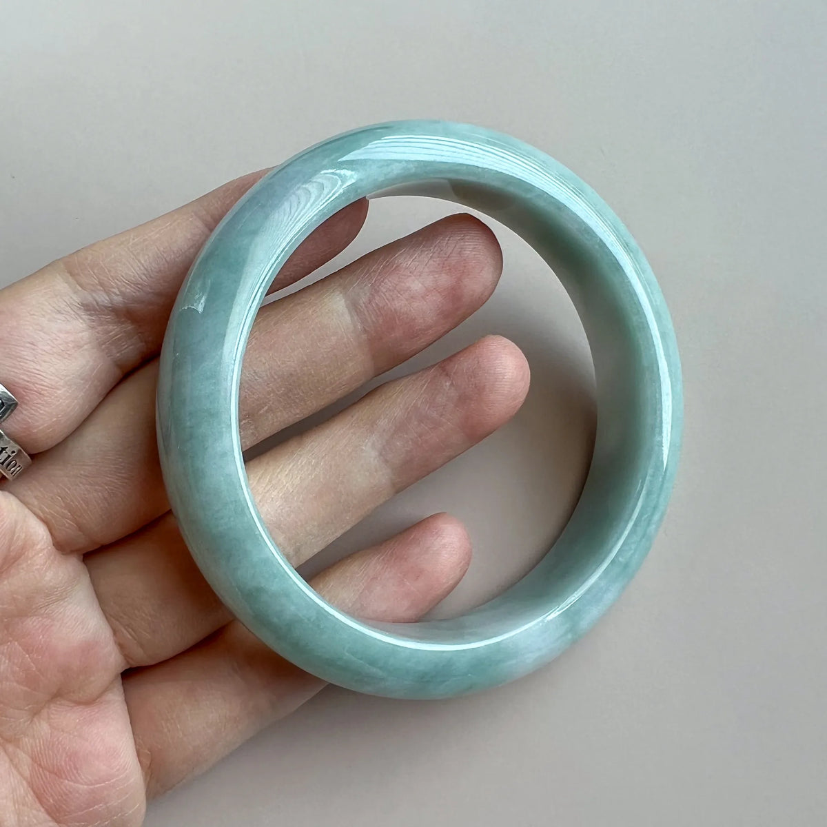 Handheld view of jade bangle with smooth glossy finish and pale green color