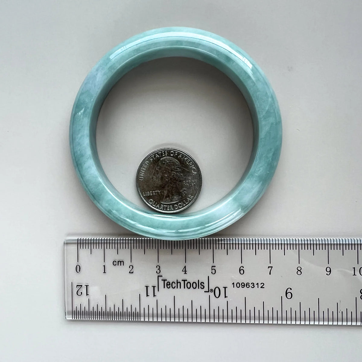 Jade bangle with coin and ruler for size reference, polished translucent stone