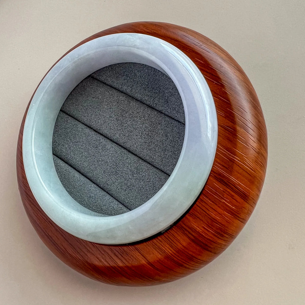 Angled view of light blue jade bangle resting on textured display case, polished finish