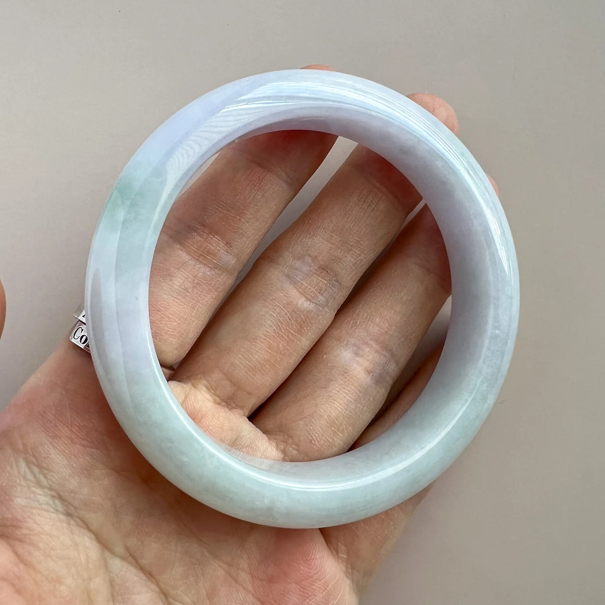 Jade bangle held in hand, showing smooth rounded profile and translucent polished finish