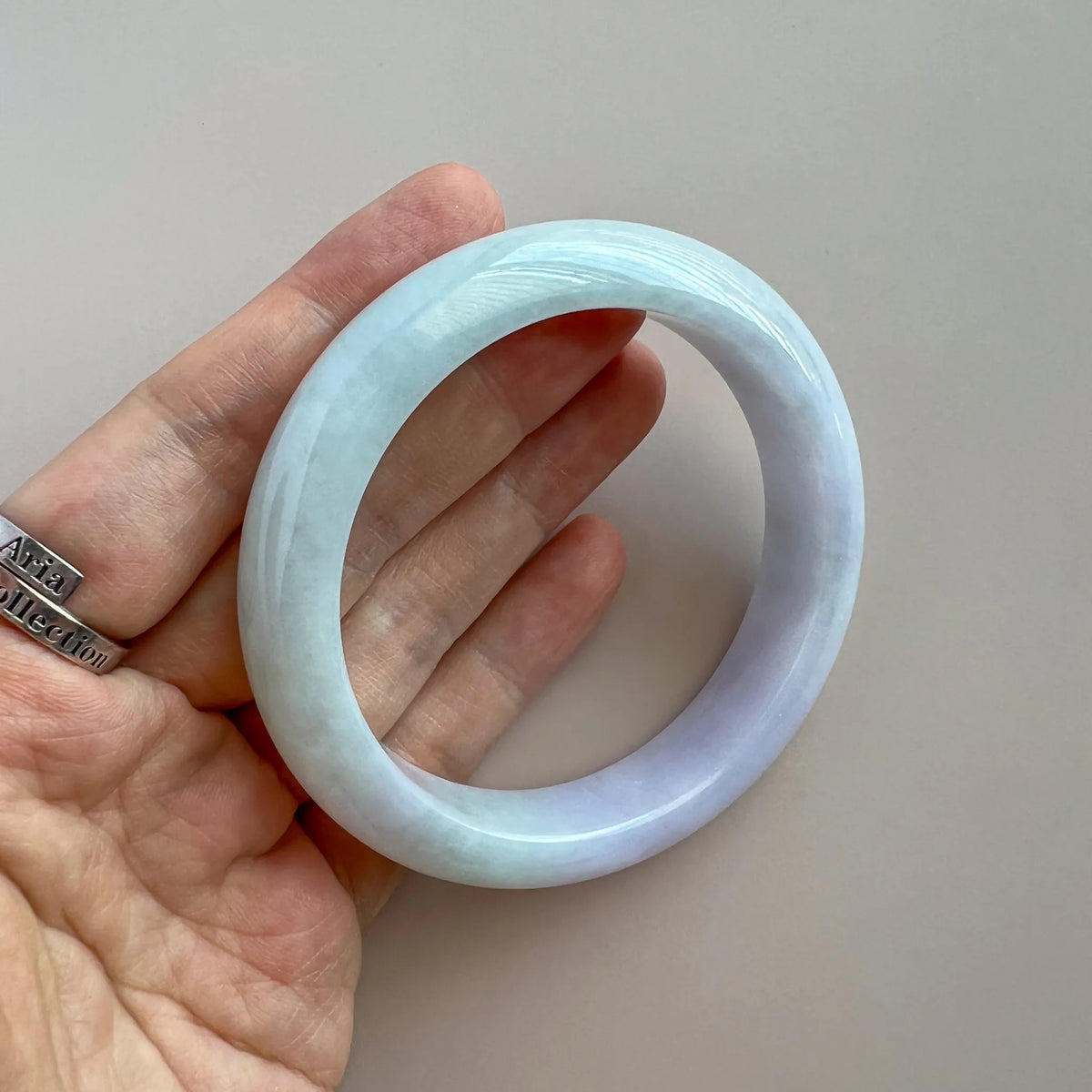 Handheld angled view of translucent jade bangle with smooth rounded edges and glossy finish