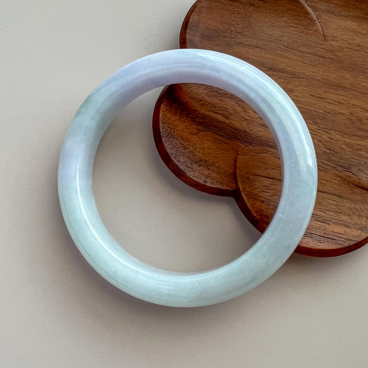 Jade bangle on neutral surface with wooden stand, polished round form and pale blue color