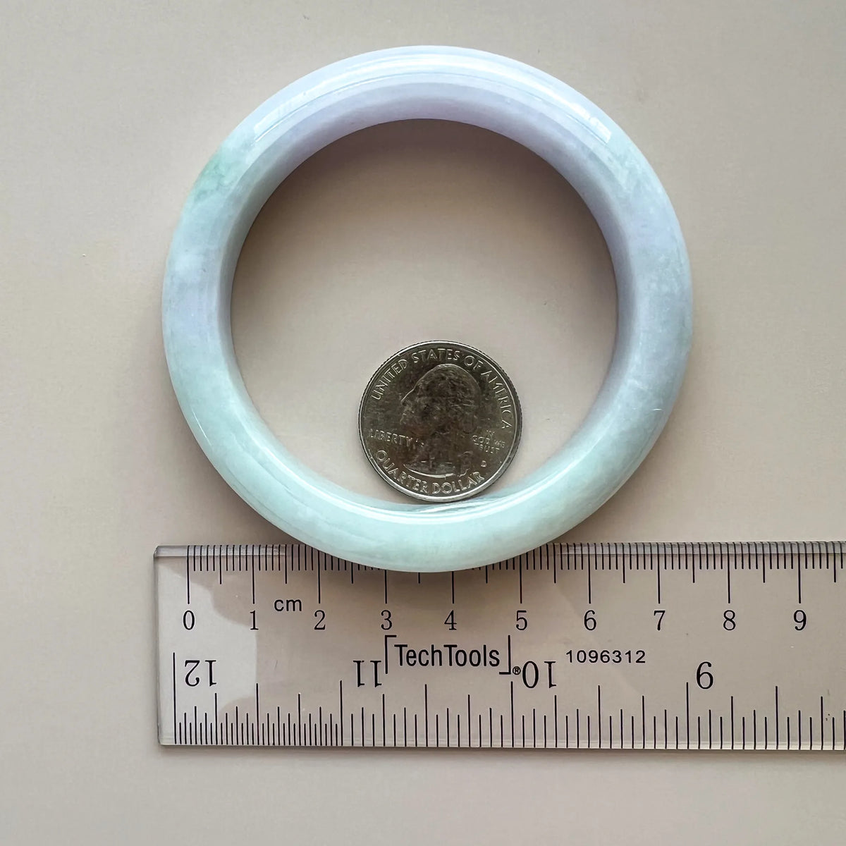 Top view of pale blue-green jadeite bangle beside a ruler and coin, showing its inner opening and polished surface