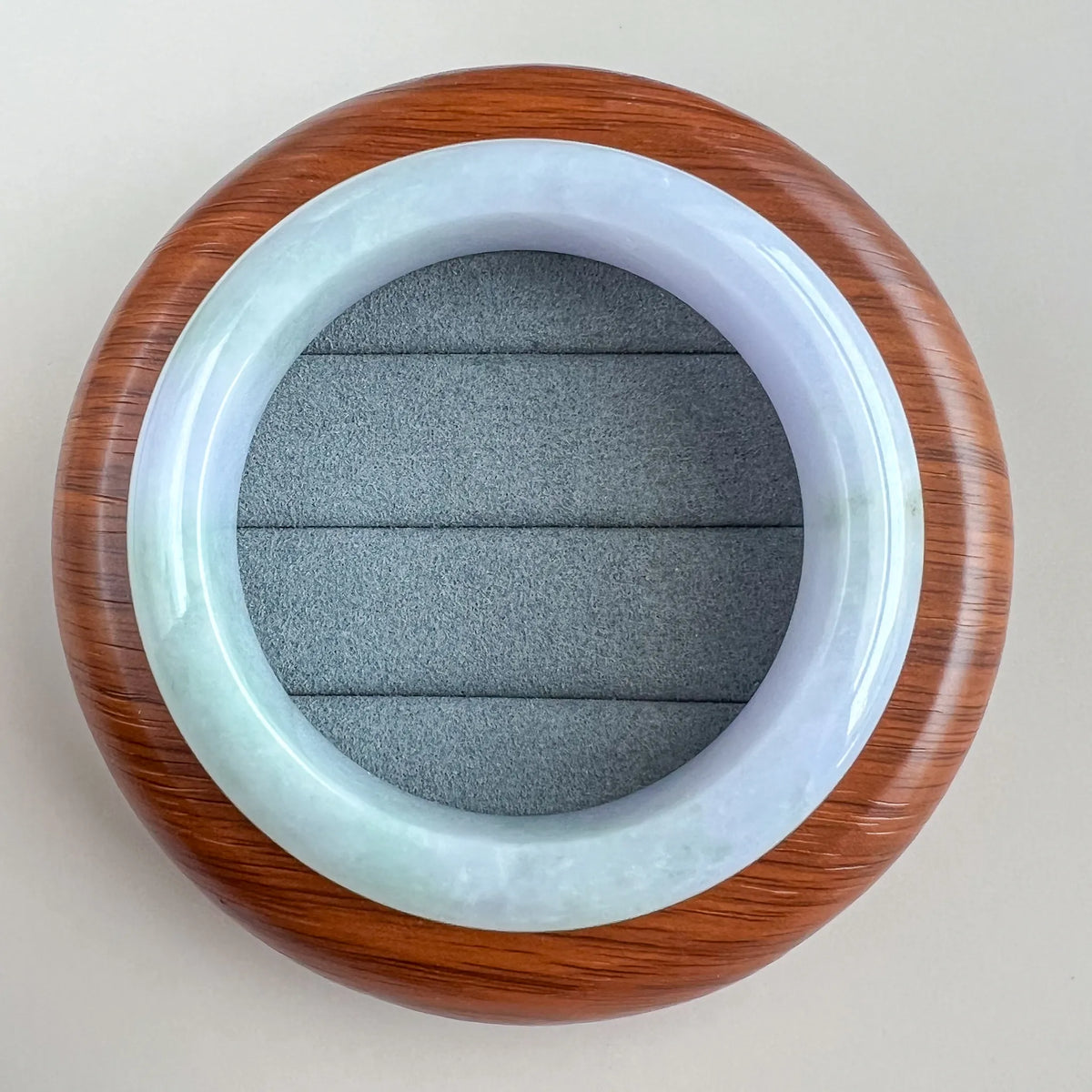 Top view of glossy jade bangle resting on wooden display base with cushioned insert