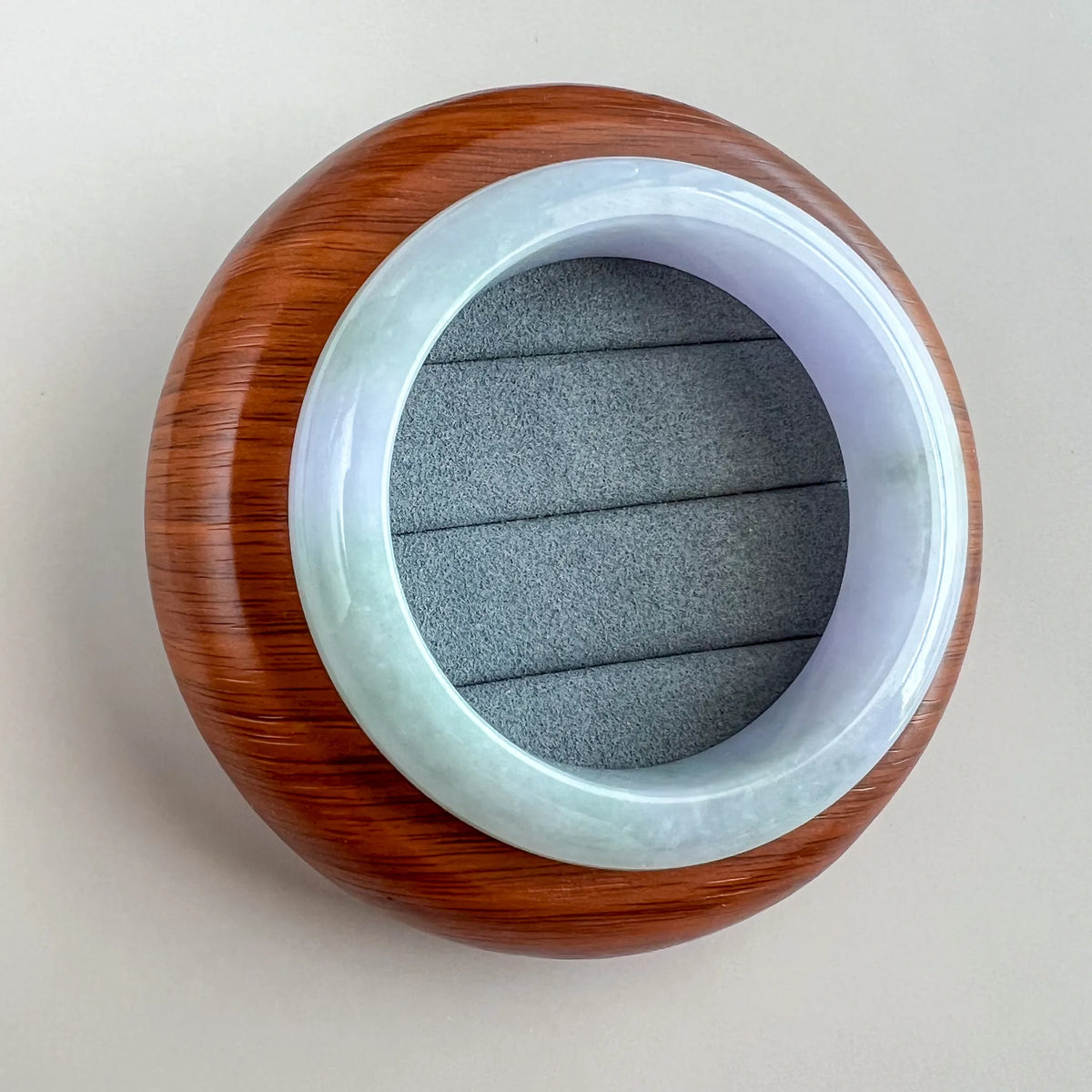 Centered top view of polished jade bangle on wooden display base with cushioned insert