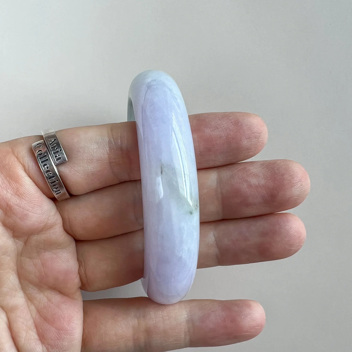 Angled side view of polished jade bangle with subtle green inclusions on hand