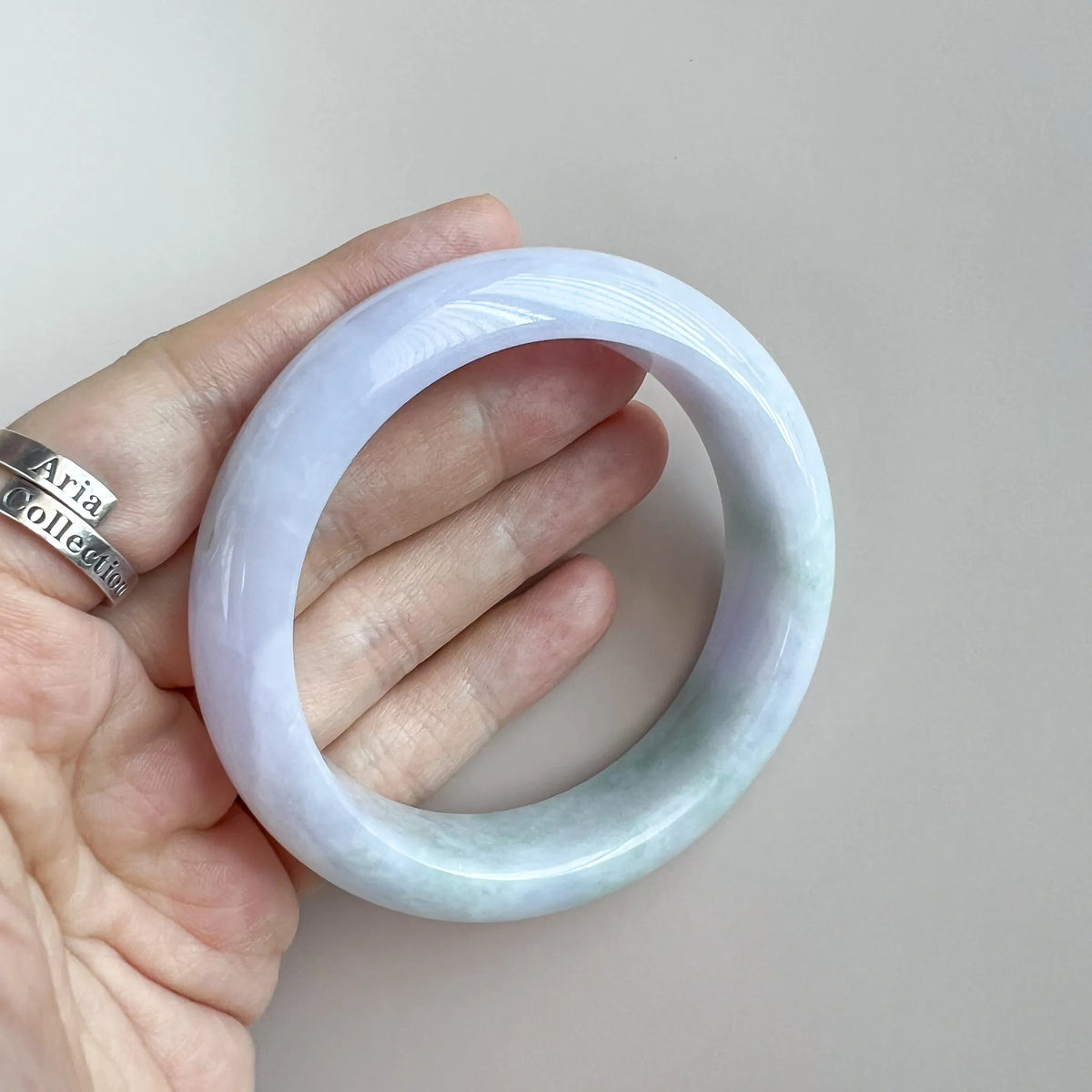 Handheld front view of glossy pale jade bangle with soft lavender and mint tones