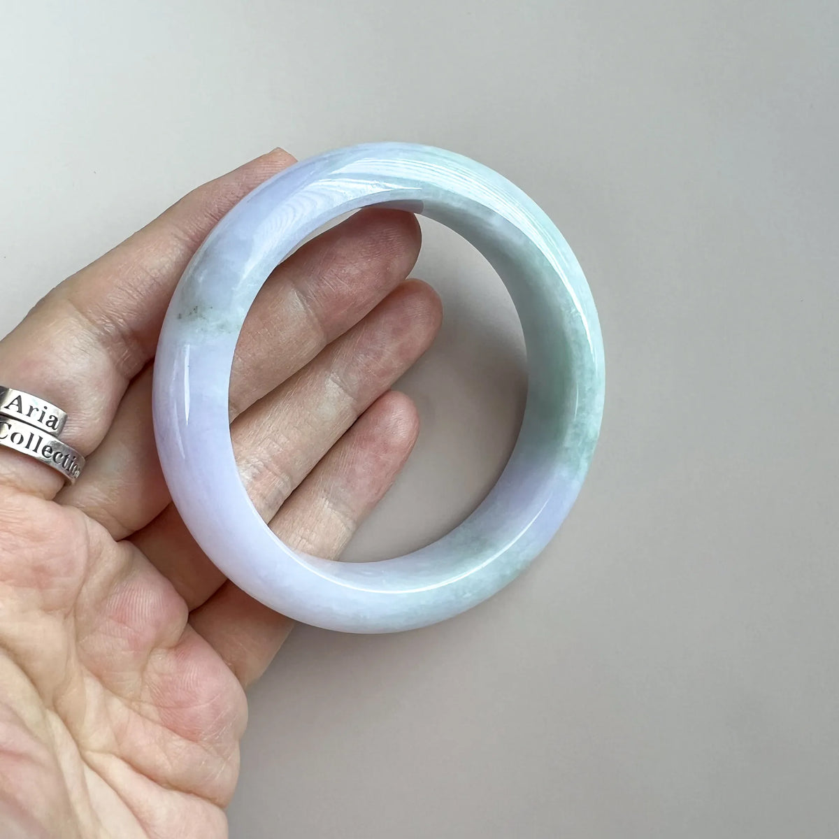 Angled handheld view of polished jade bangle with light green mottling