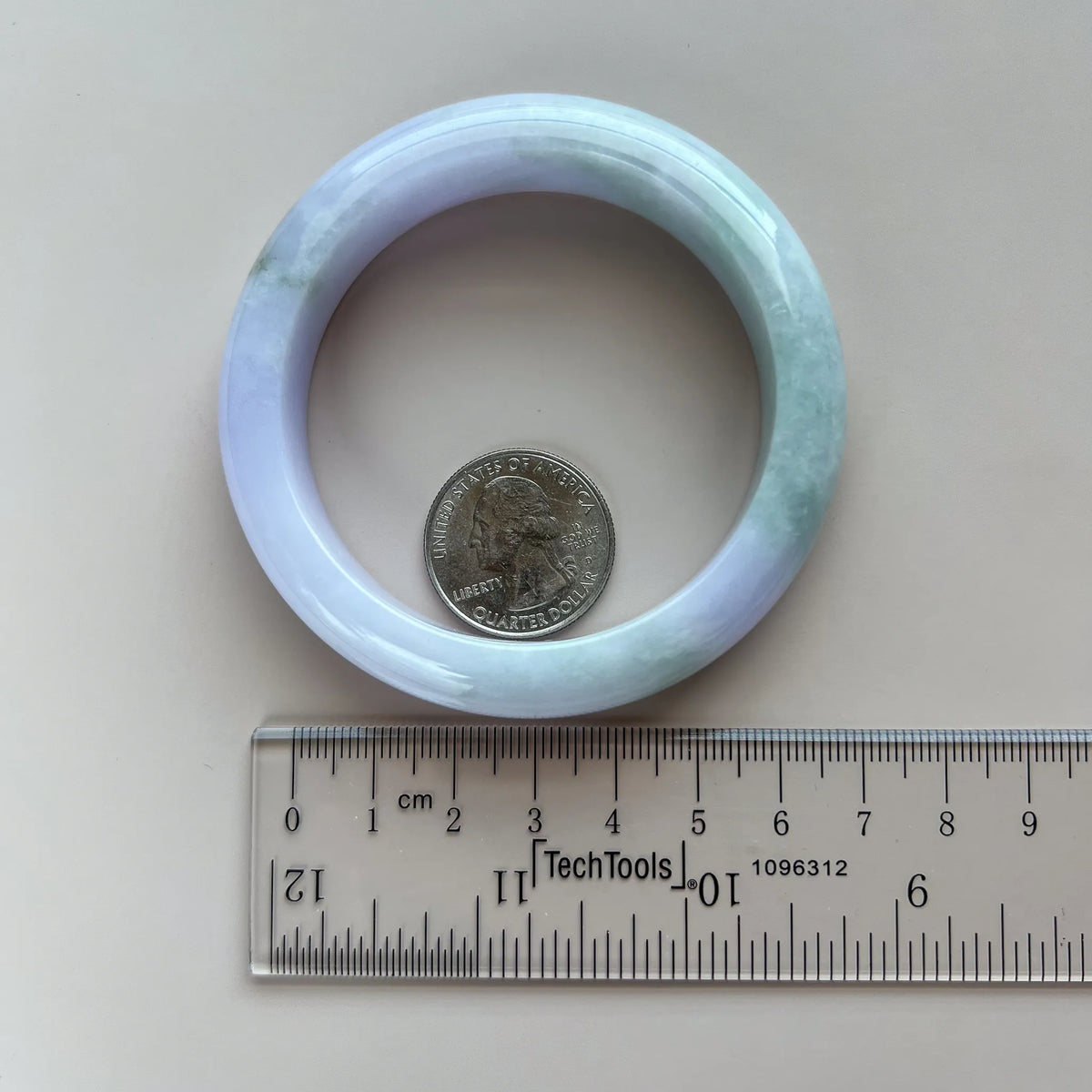 Jade bangle shown with ruler and quarter for size reference on white background