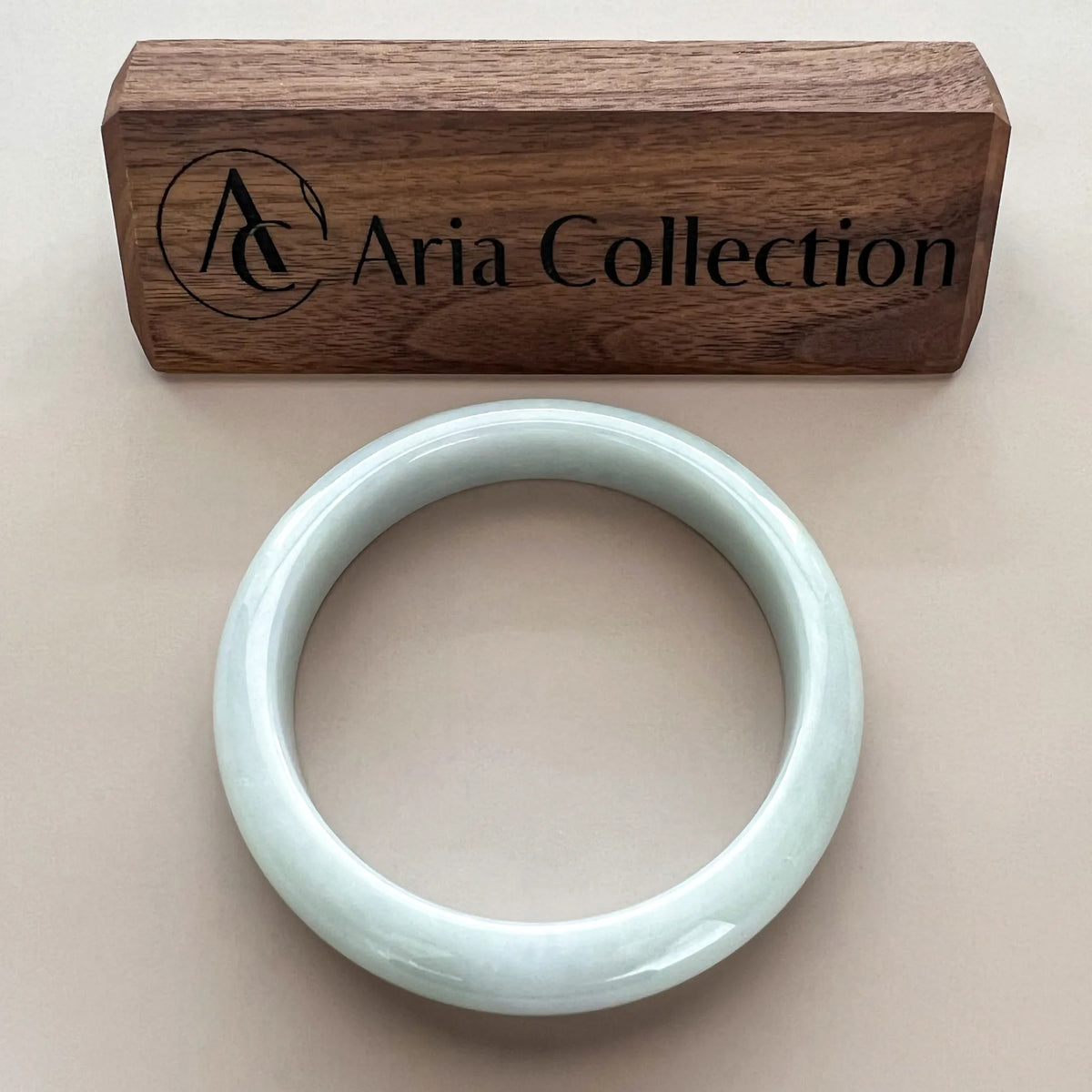 Front view of pale jade bangle on beige background with branded wooden box