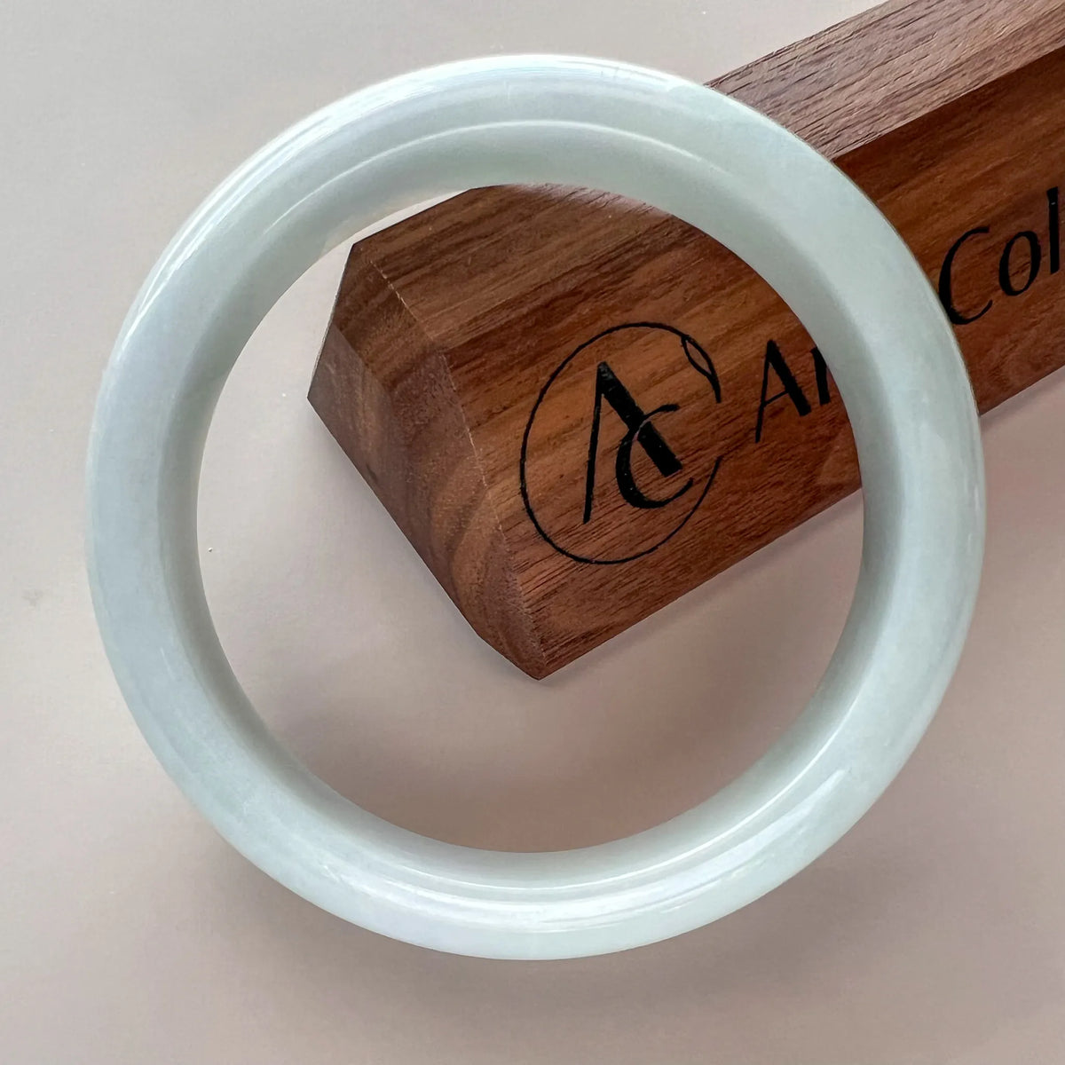 Glossy pale jade bangle angled over branded wooden display box
