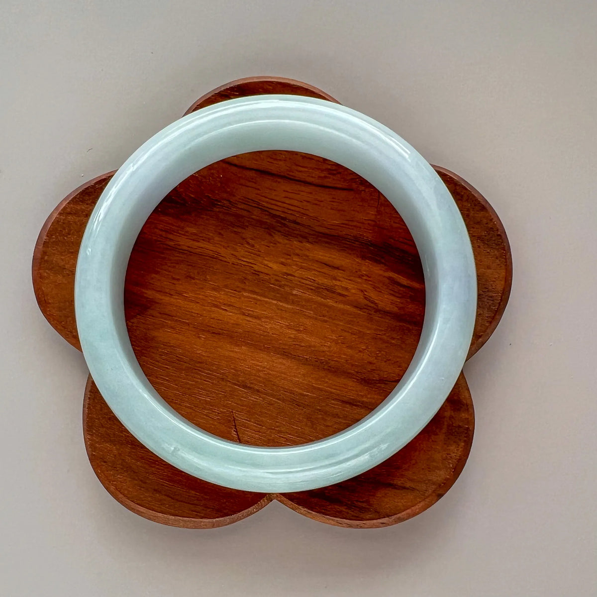 Polished jade bangle on flower-shaped wooden stand, top view