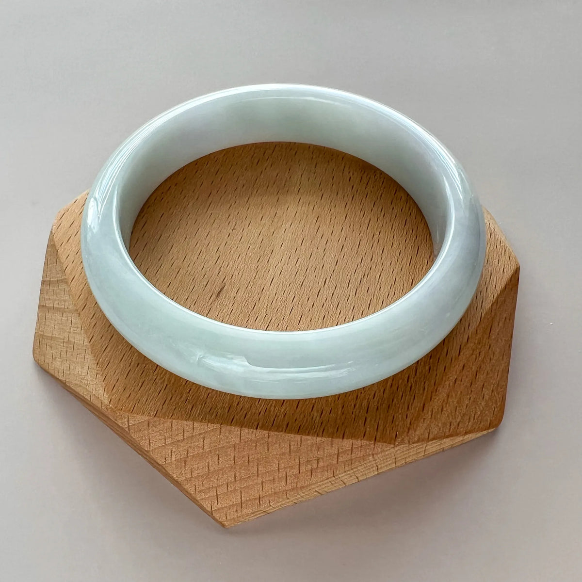 Glossy jade bangle displayed on faceted wooden base, top view