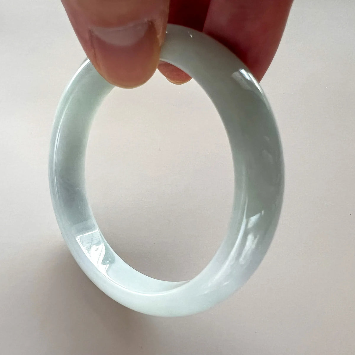 Handheld close-up of pale jade bangle showing glossy curved profile