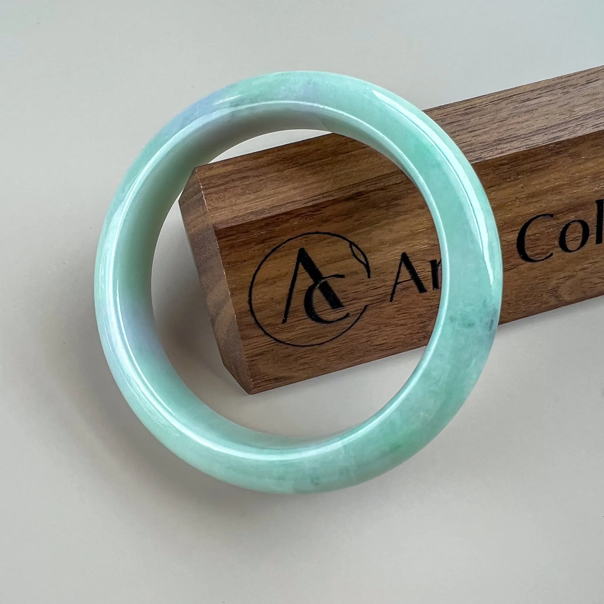 Glossy pale green jade bangle shown front-on against a wooden display block