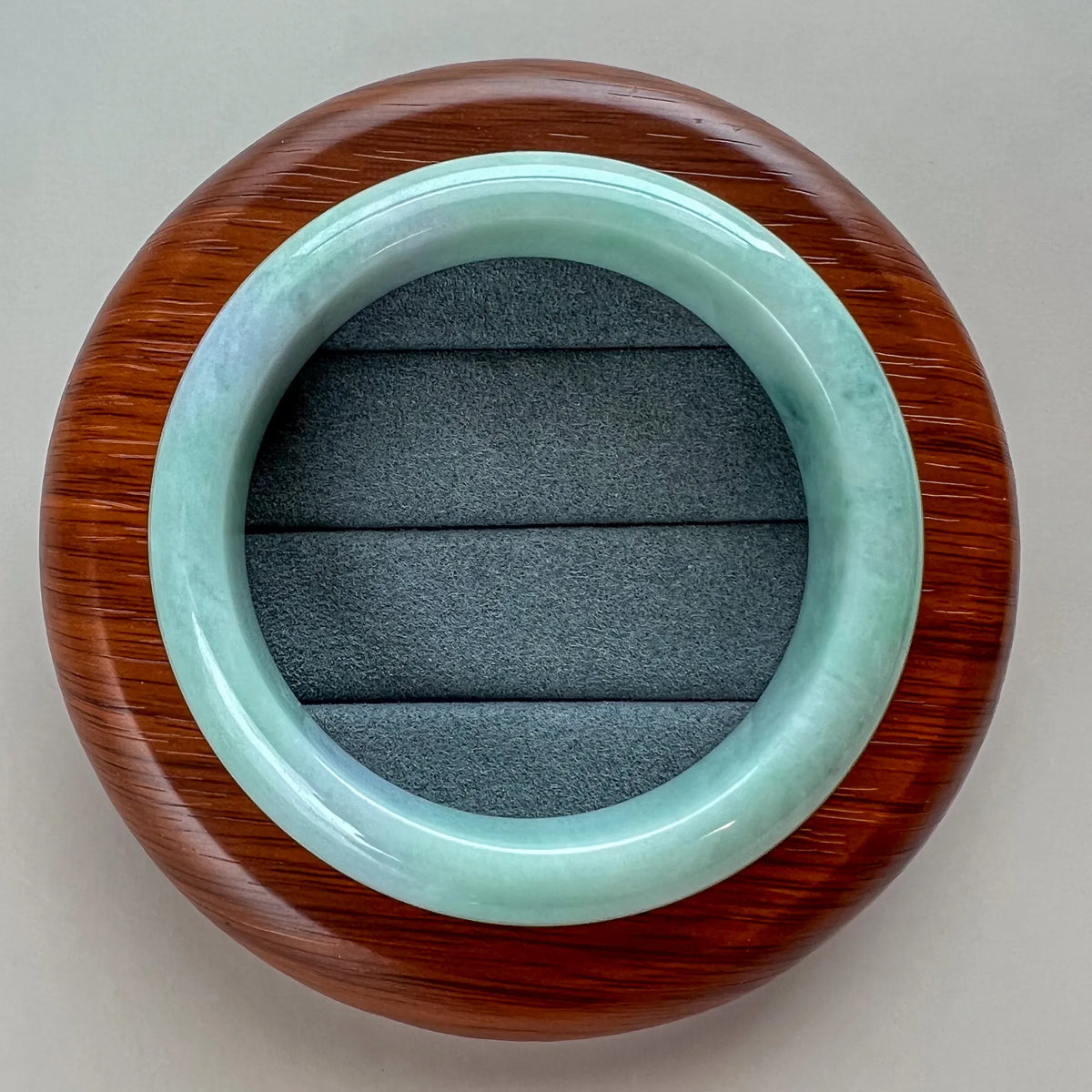 Top view of polished jade bangle on a round wooden stand with padded insert