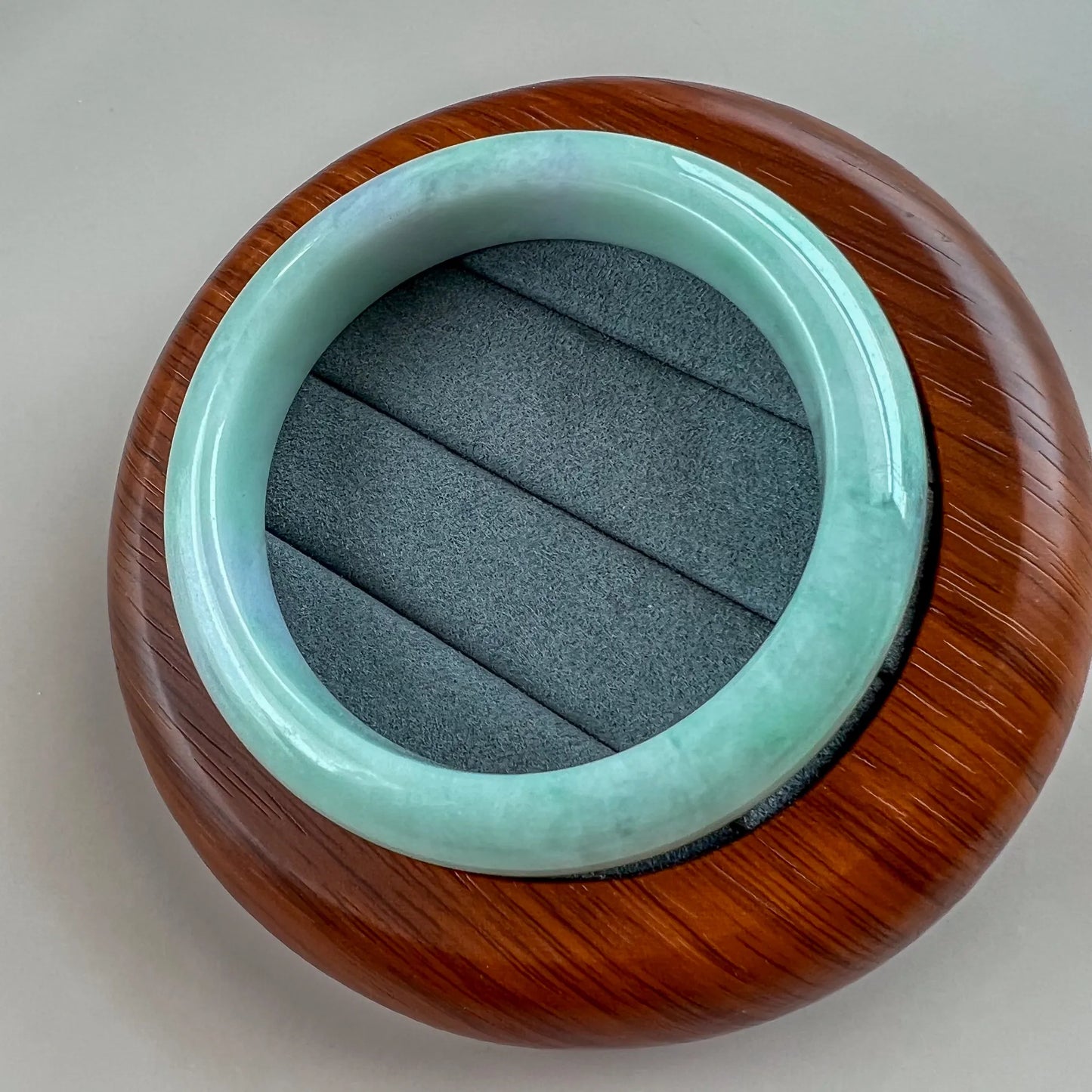 Angled view of smooth jade bangle resting on a carved wooden display base
