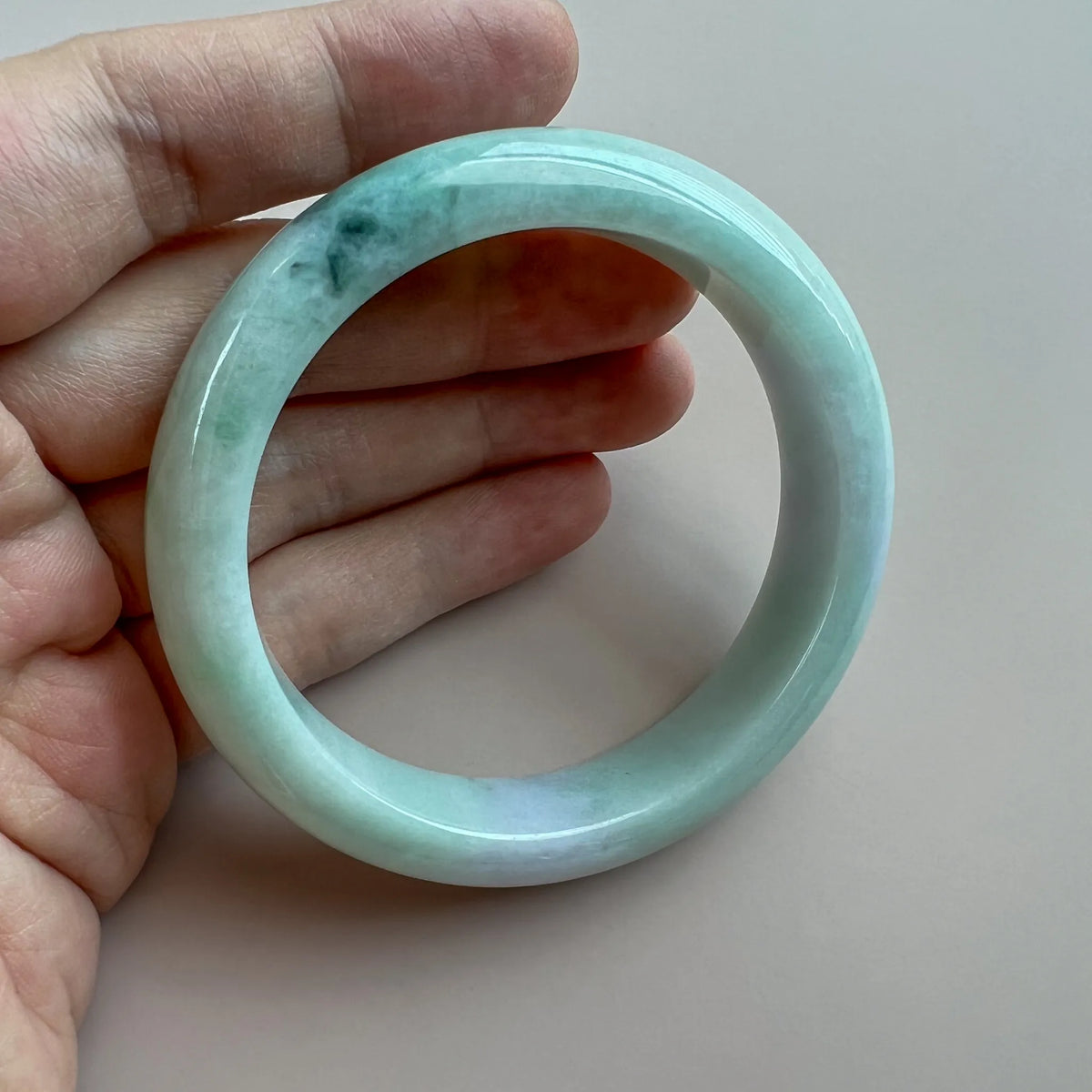 Hand-held view of translucent jade bangle with natural dark inclusions