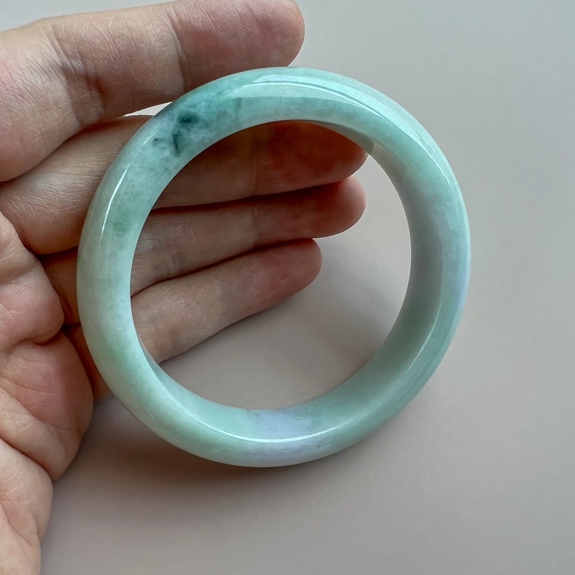 Hand-held view of translucent jade bangle with natural dark inclusions