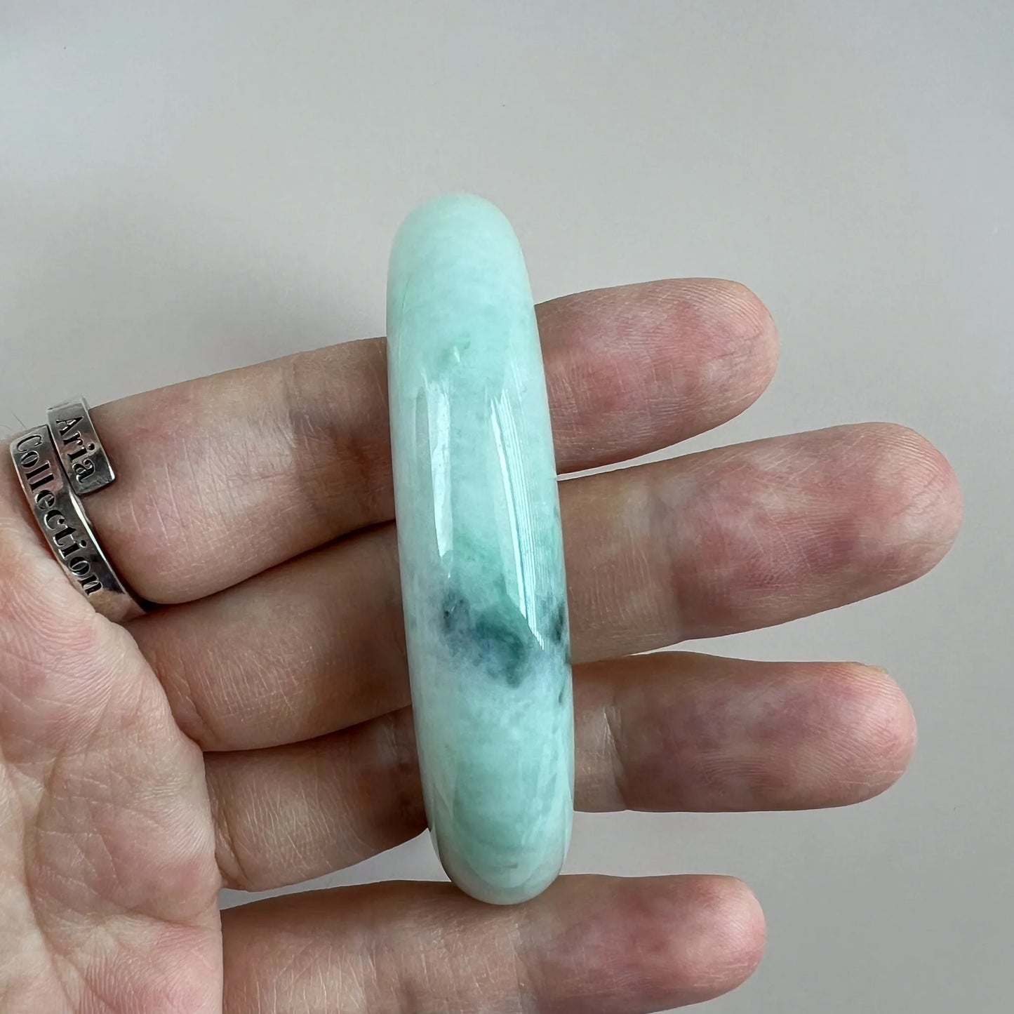 Side profile of polished jade bangle shown on fingers for scale