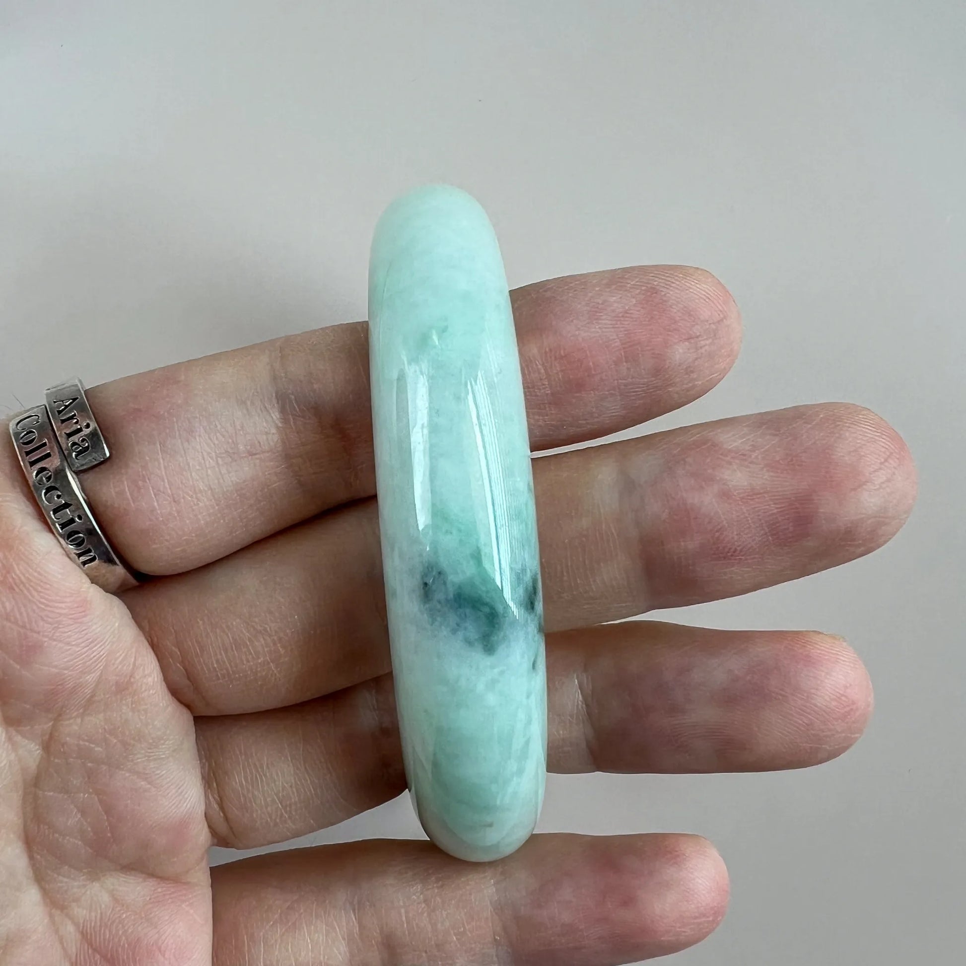 Side profile of polished jade bangle shown on fingers for scale