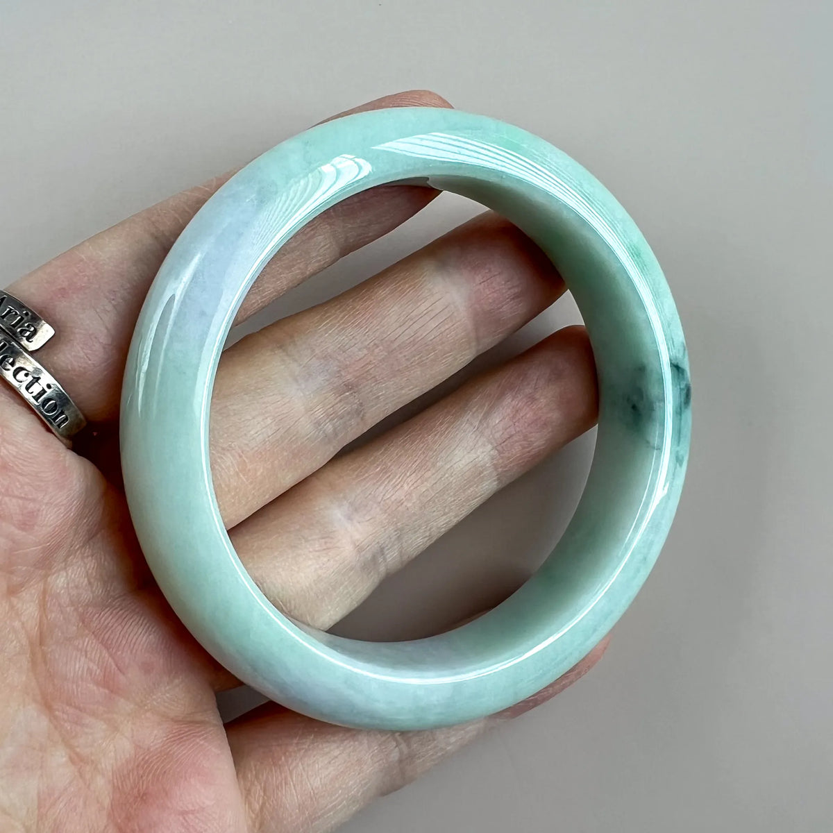 Close hand-held view of smooth jade bangle with glossy finish and mottled color