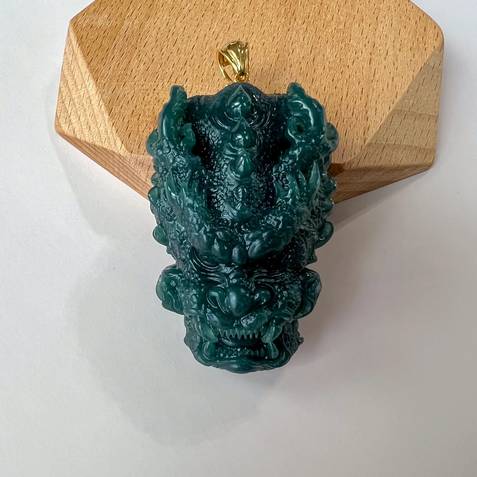 Front view of dark green carved jade dragon pendant with gold bail on wooden display