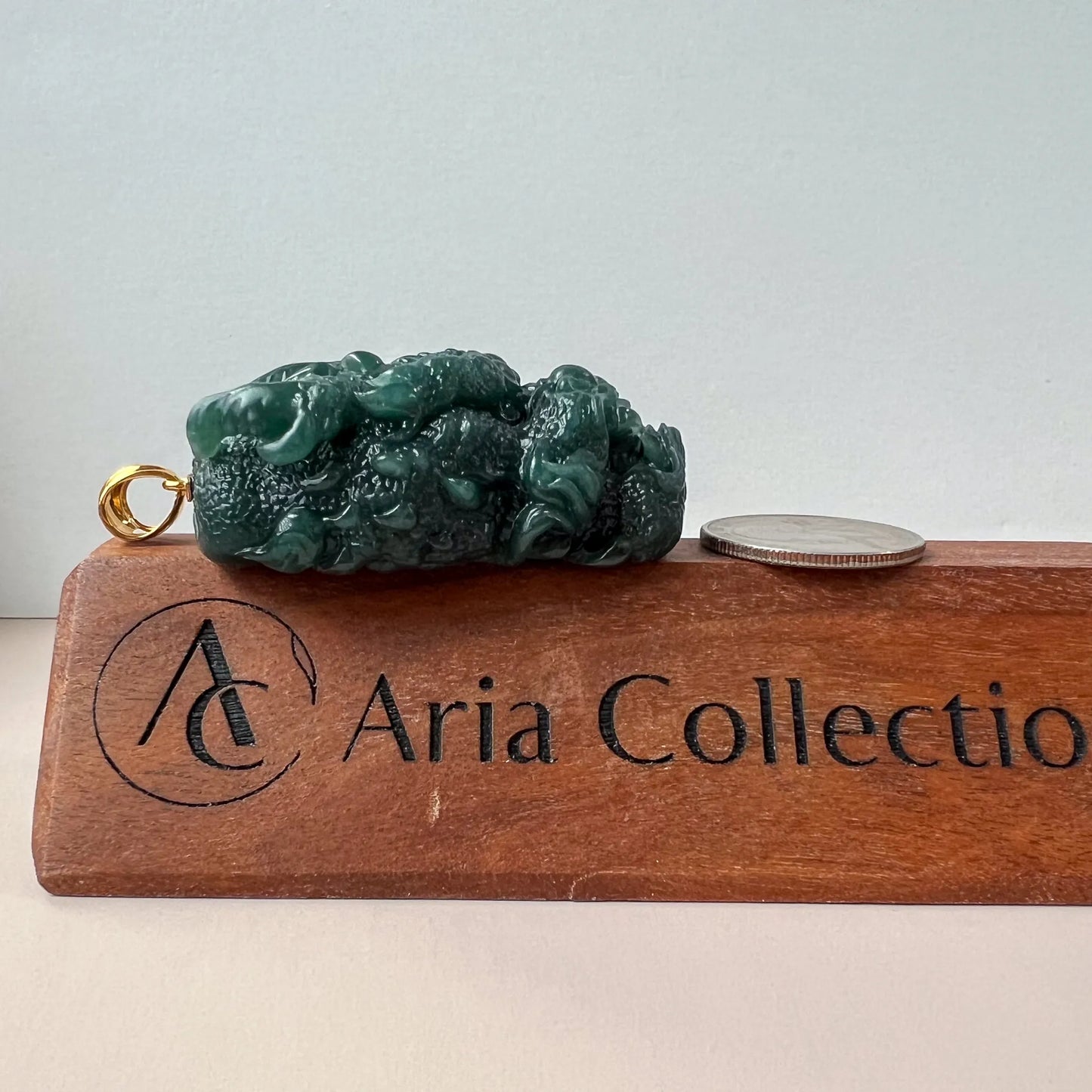 Side profile of green carved jade pendant with gold bail and size comparison on wooden stand
