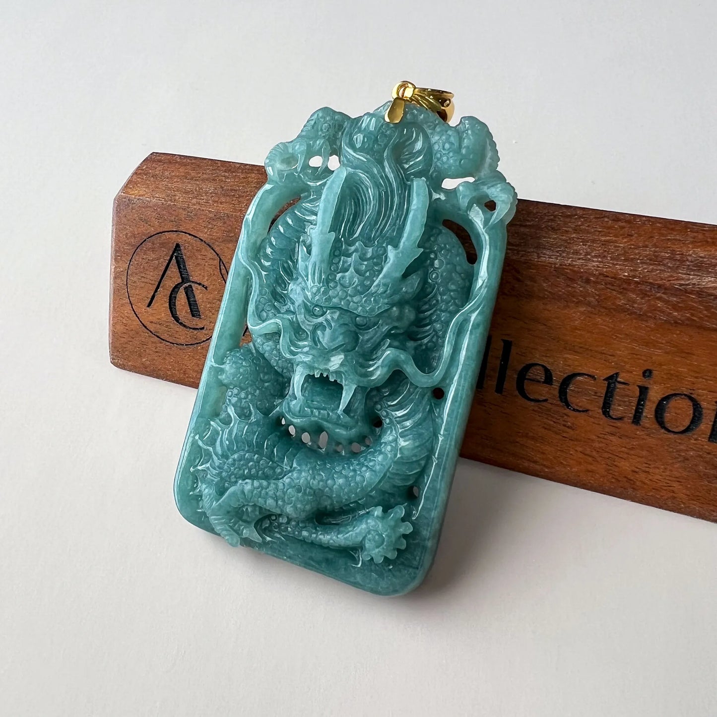 Angled front view of glossy carved jade dragon pendant on wooden stand
