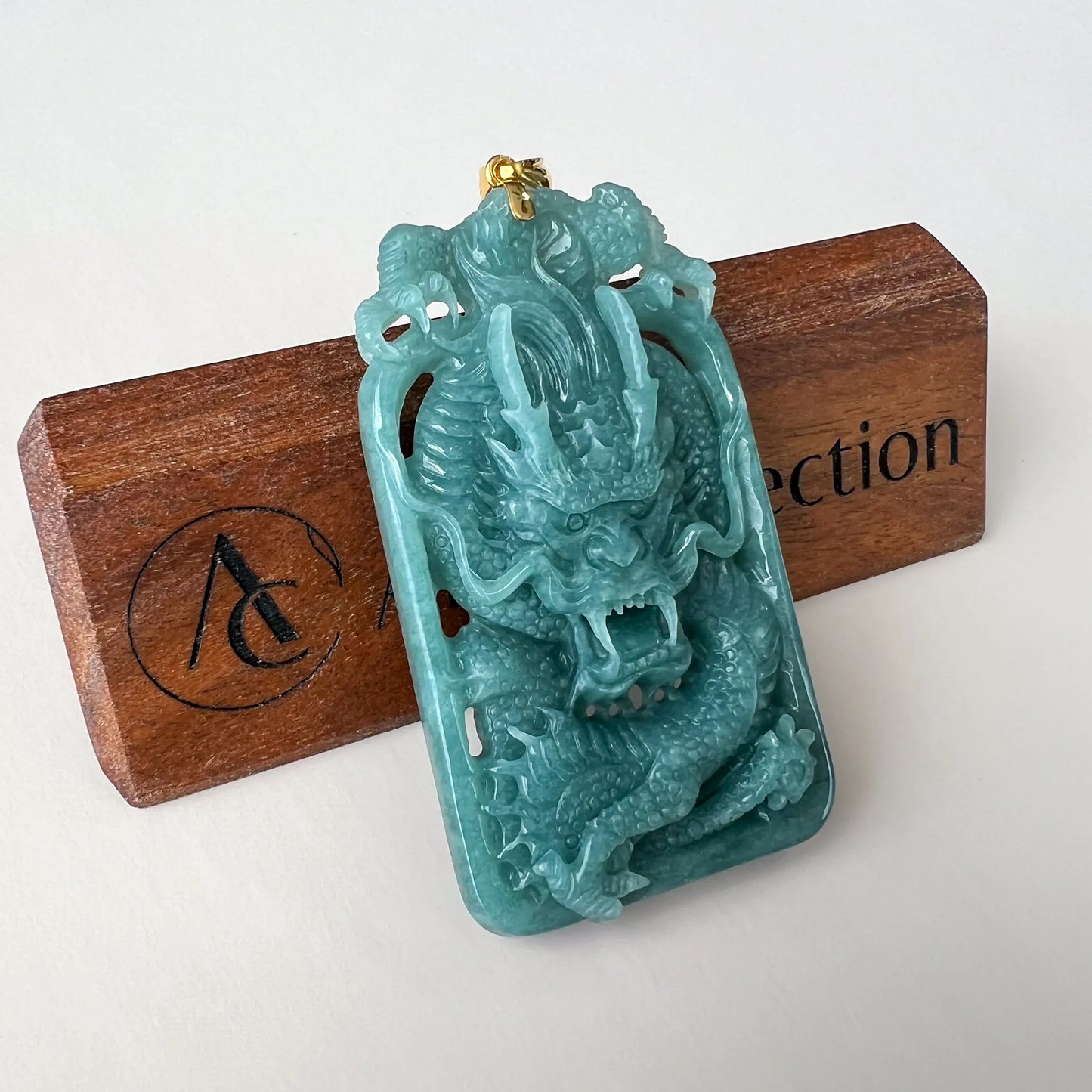 Three-quarter front view of translucent blue-green dragon pendant with gold bail