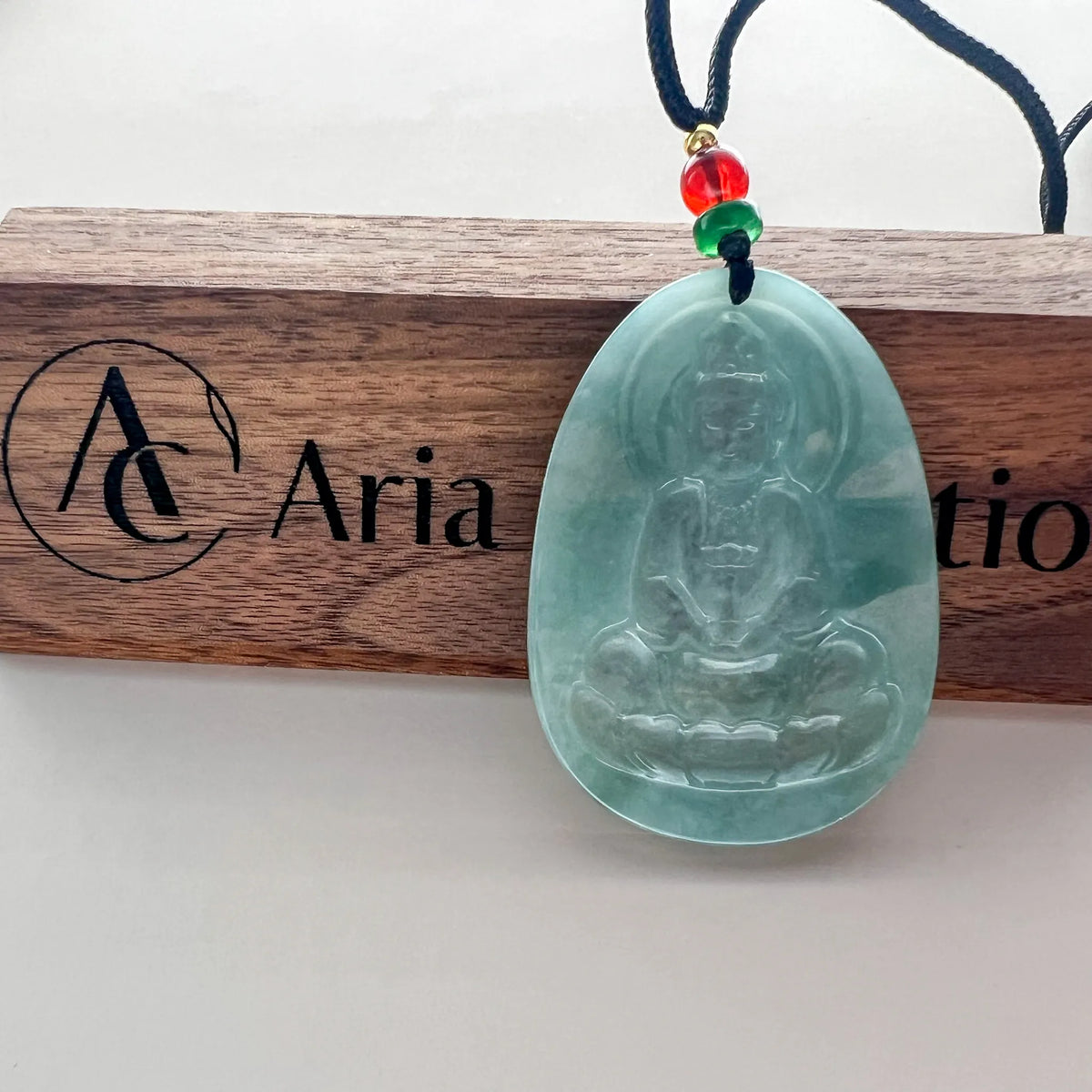 Front view jade pendant on display plaque with carved Buddha and cord