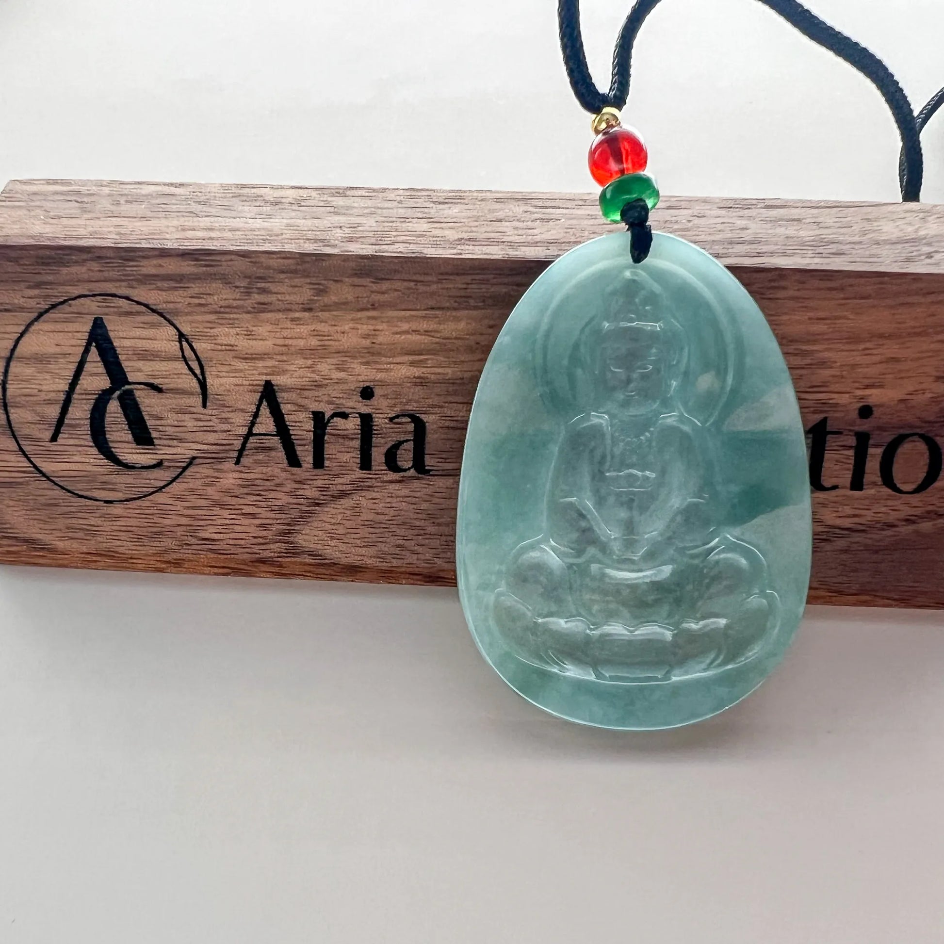 Front view jade pendant on display plaque with carved Buddha and cord