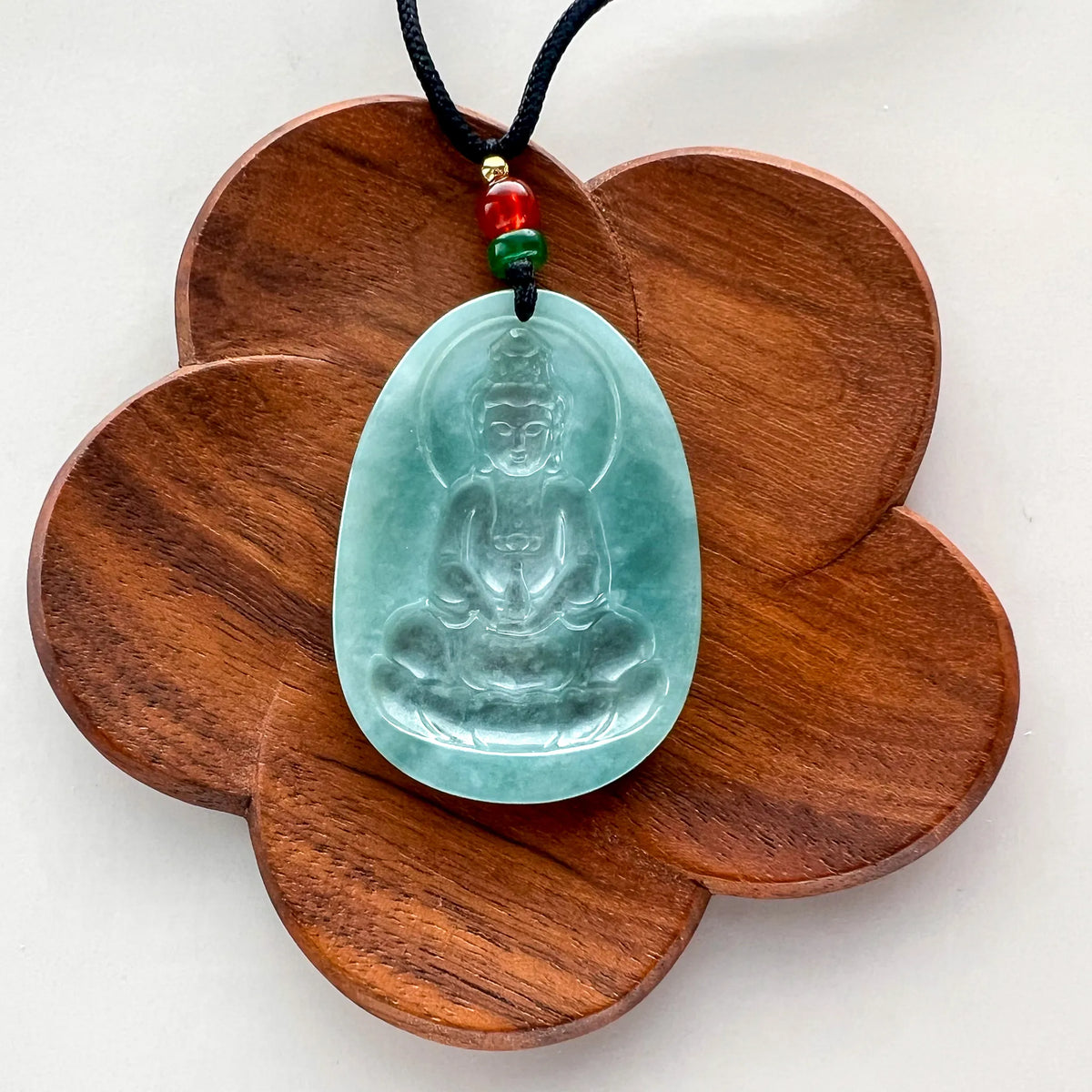 Carved jade Buddha pendant on wooden flower display, front-facing view