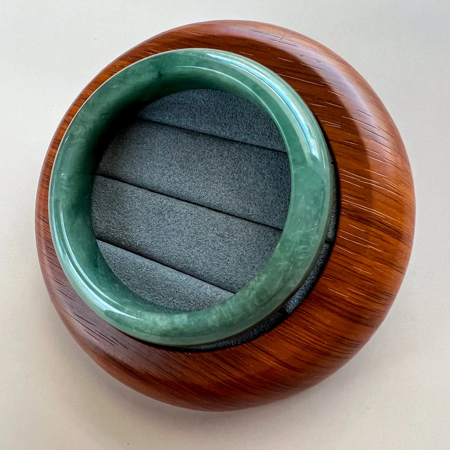 Angled view of polished green jade bangle on carved wooden display base