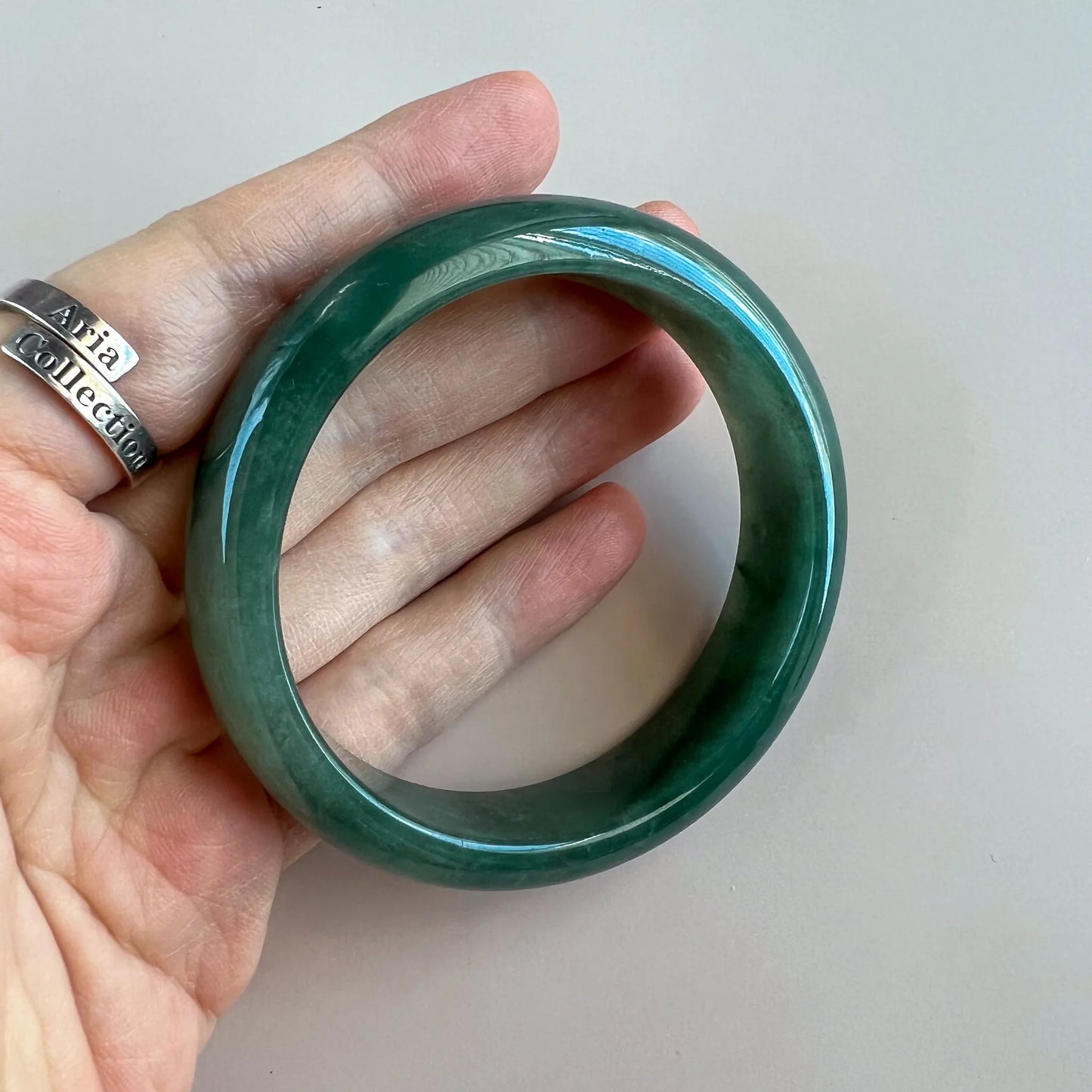 Handheld view of glossy green jade bangle showing smooth round profile