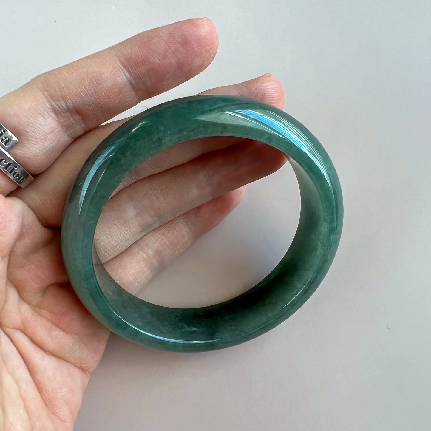Handheld angled view of polished green jade bangle with translucent stone finish