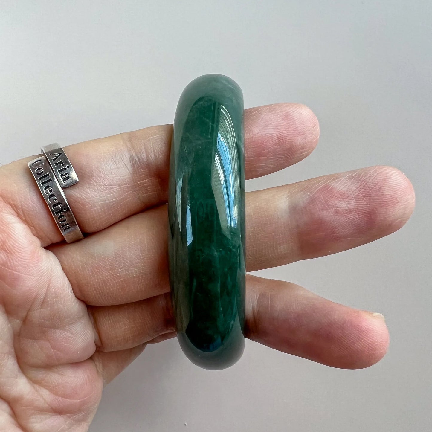 Side profile of thick polished green jade bangle held between fingers