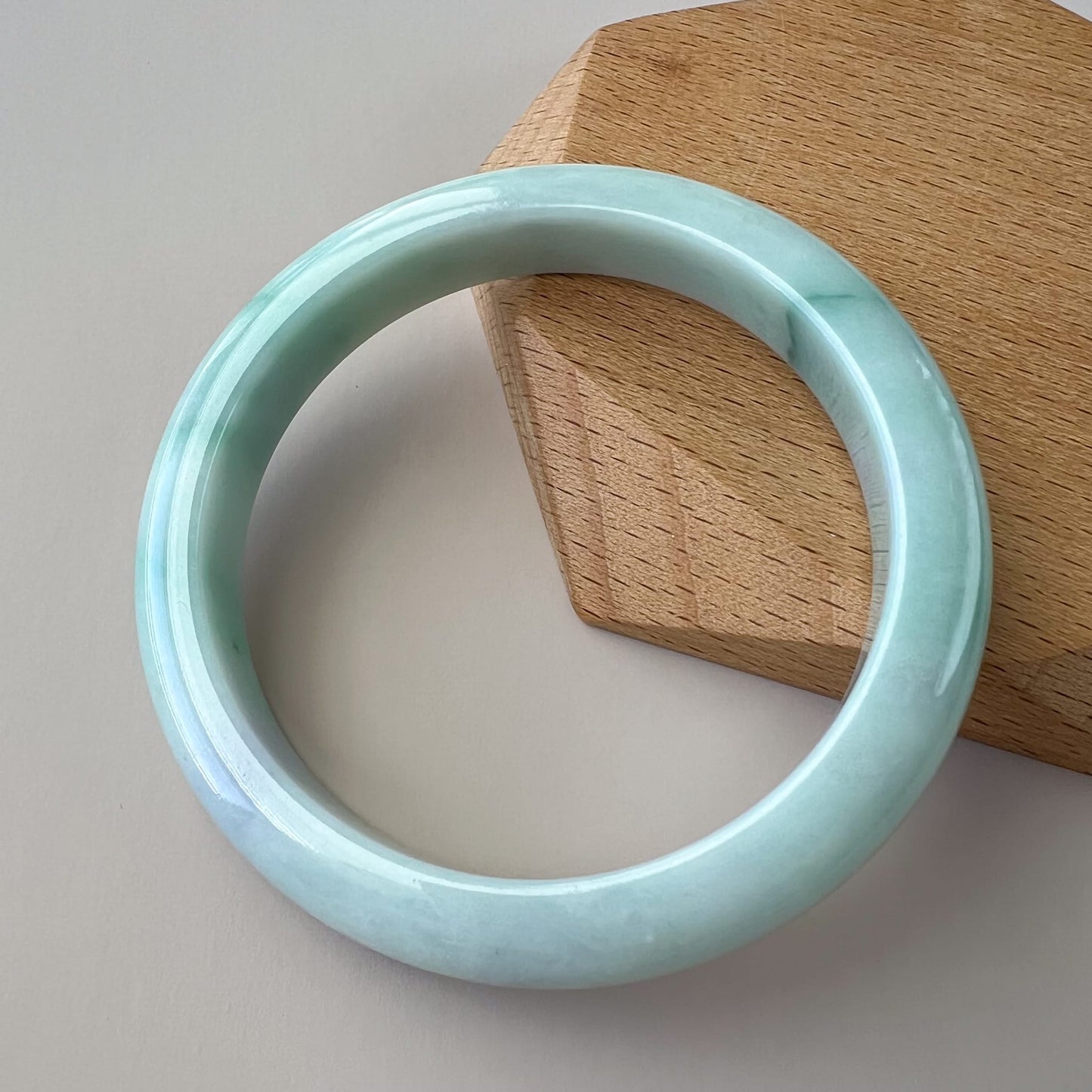 Light green jadeite bangle with glossy finish, angled on wood stand, showing smooth inner-flat profile and texture