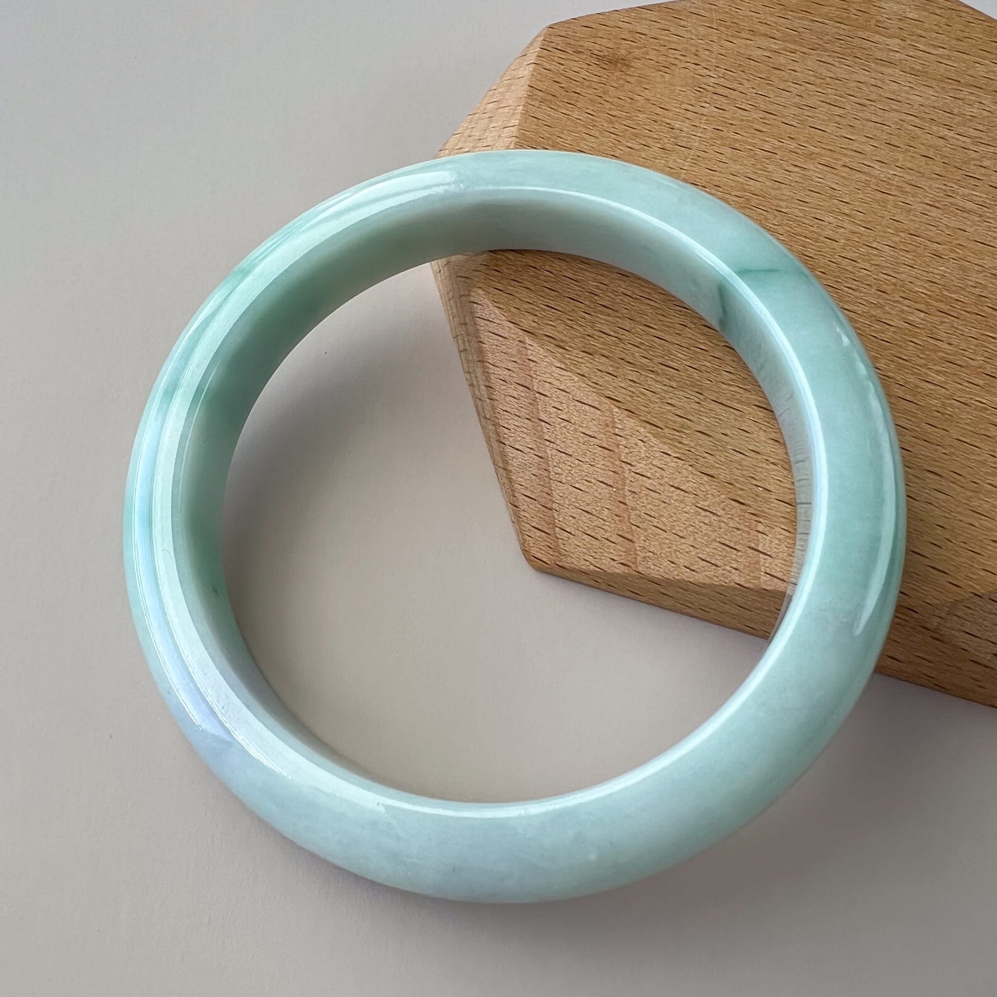 Light green jadeite bangle with glossy finish, angled on wood stand, showing smooth inner-flat profile and texture