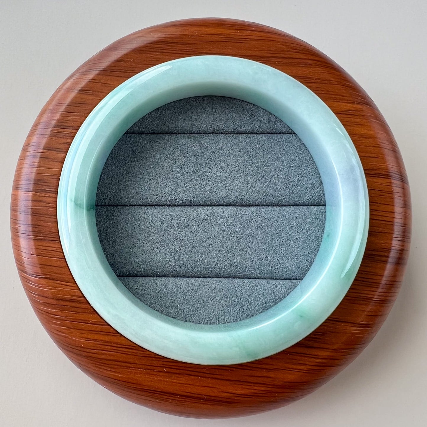 Top-down view of light green Burmese Type A jadeite bangle with glossy finish on gray velvet display cushion