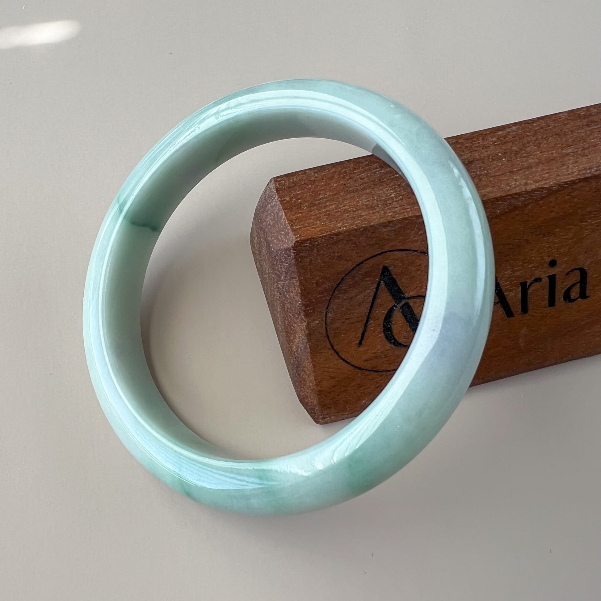 Light green Burmese Type A jadeite jade bangle, inner-flat profile, glossy finish, angled close-up on wood stand
