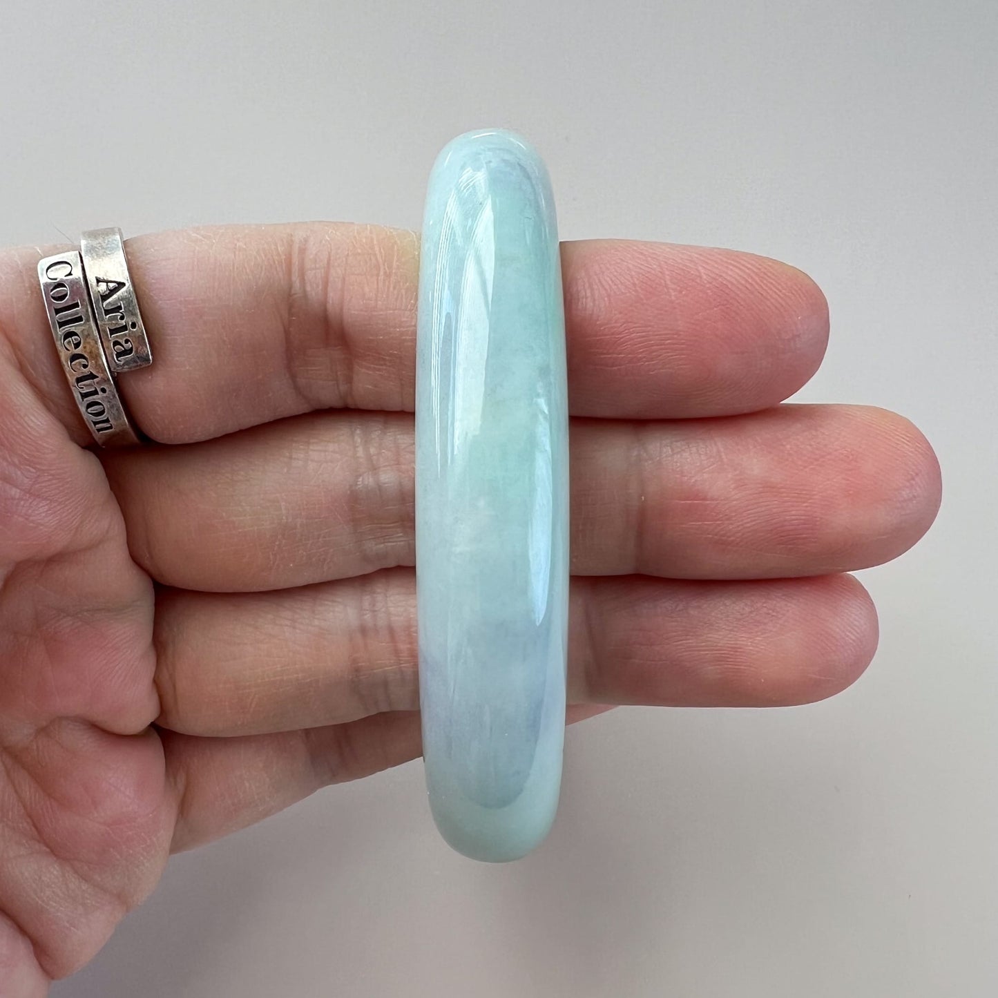 Light green Burmese Type A jadeite jade inner-flat bangle, glossy polished finish, held in hand close-up