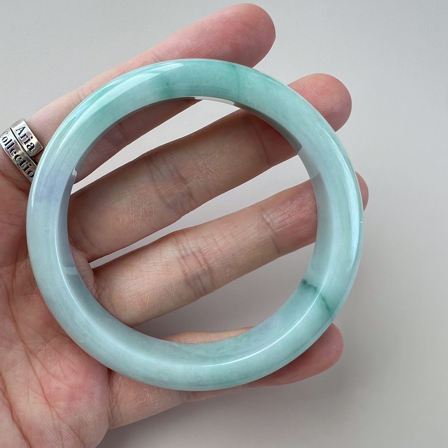 Light green Burmese Type A jadeite jade classic bangle, inner-flat, glossy polished finish, held in hand at angle