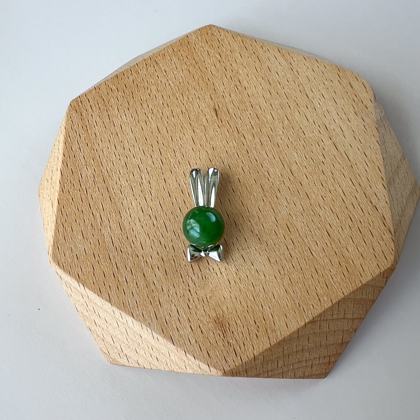 Top-down view of green nephrite jade rabbit pendant with sterling silver bowtie on a wooden display stand