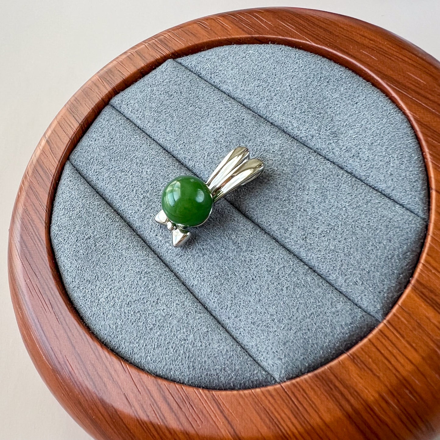 Top-down view of green nephrite jade rabbit pendant with sterling silver bowtie on gray velvet display tray